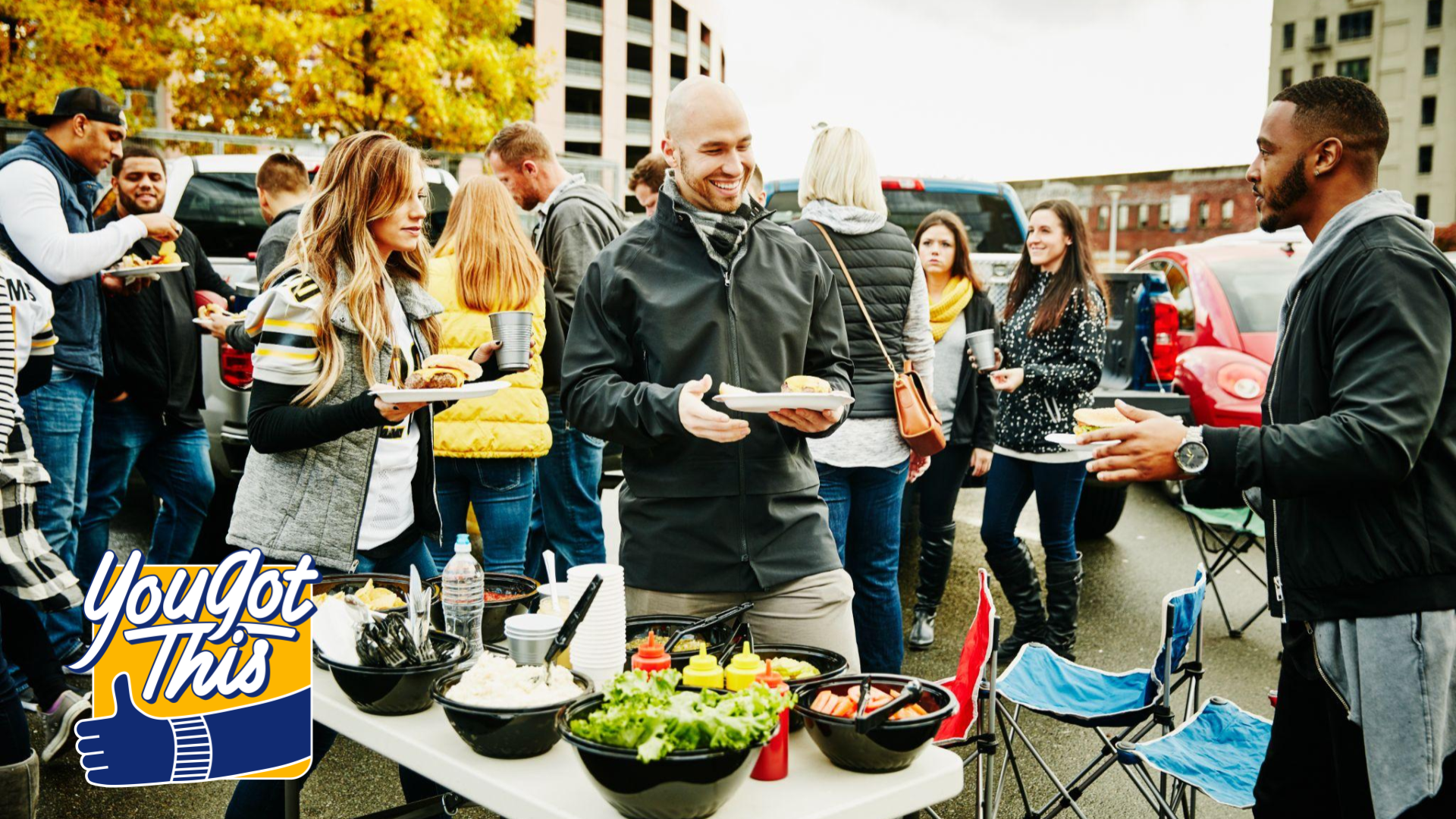 A group of football fans standing around a foot table at a tailgate party