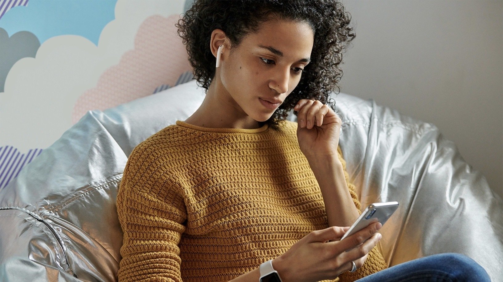 woman sitting in chair and looking at phone while wearing airpods