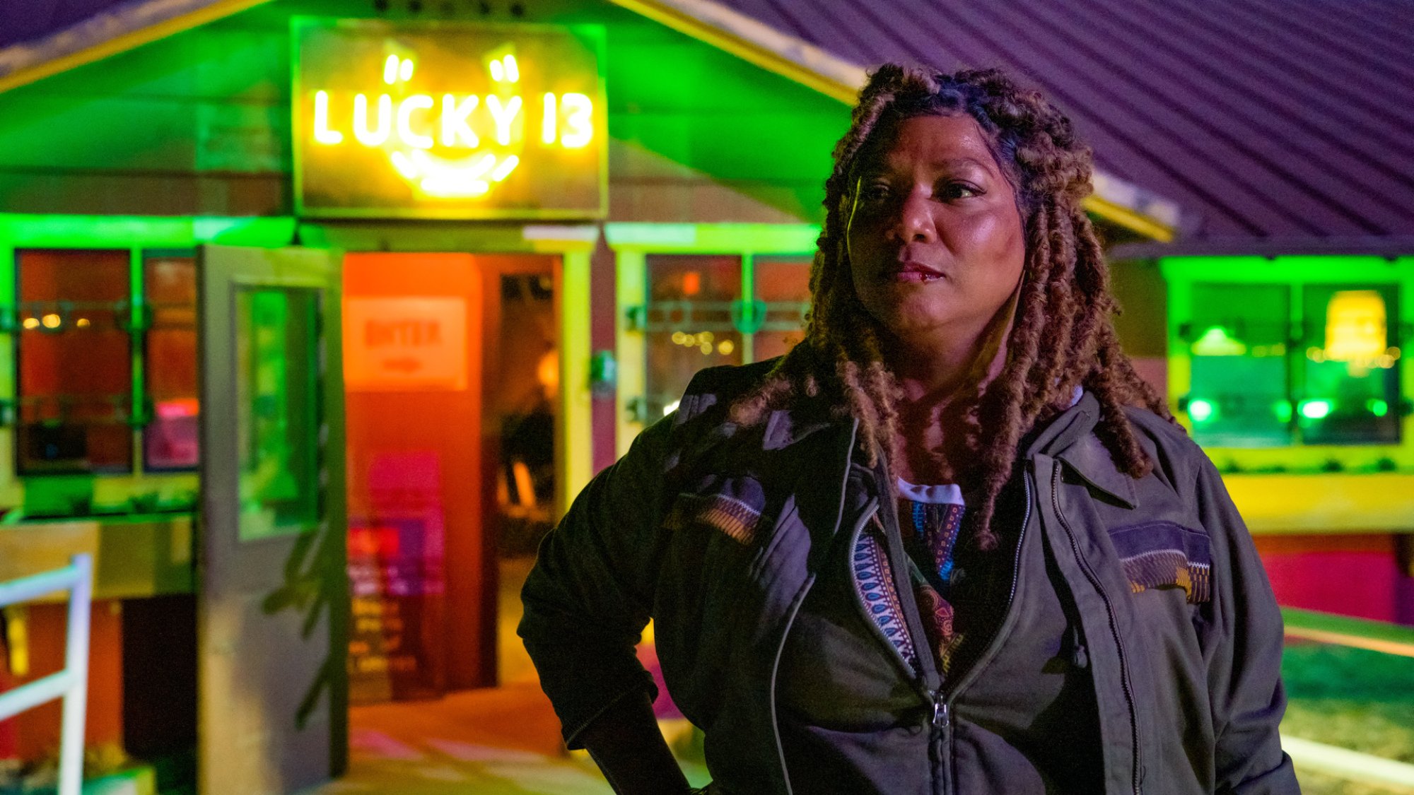 A woman stands in front of a neon lit hotel with a sign reading "Lucky 13".