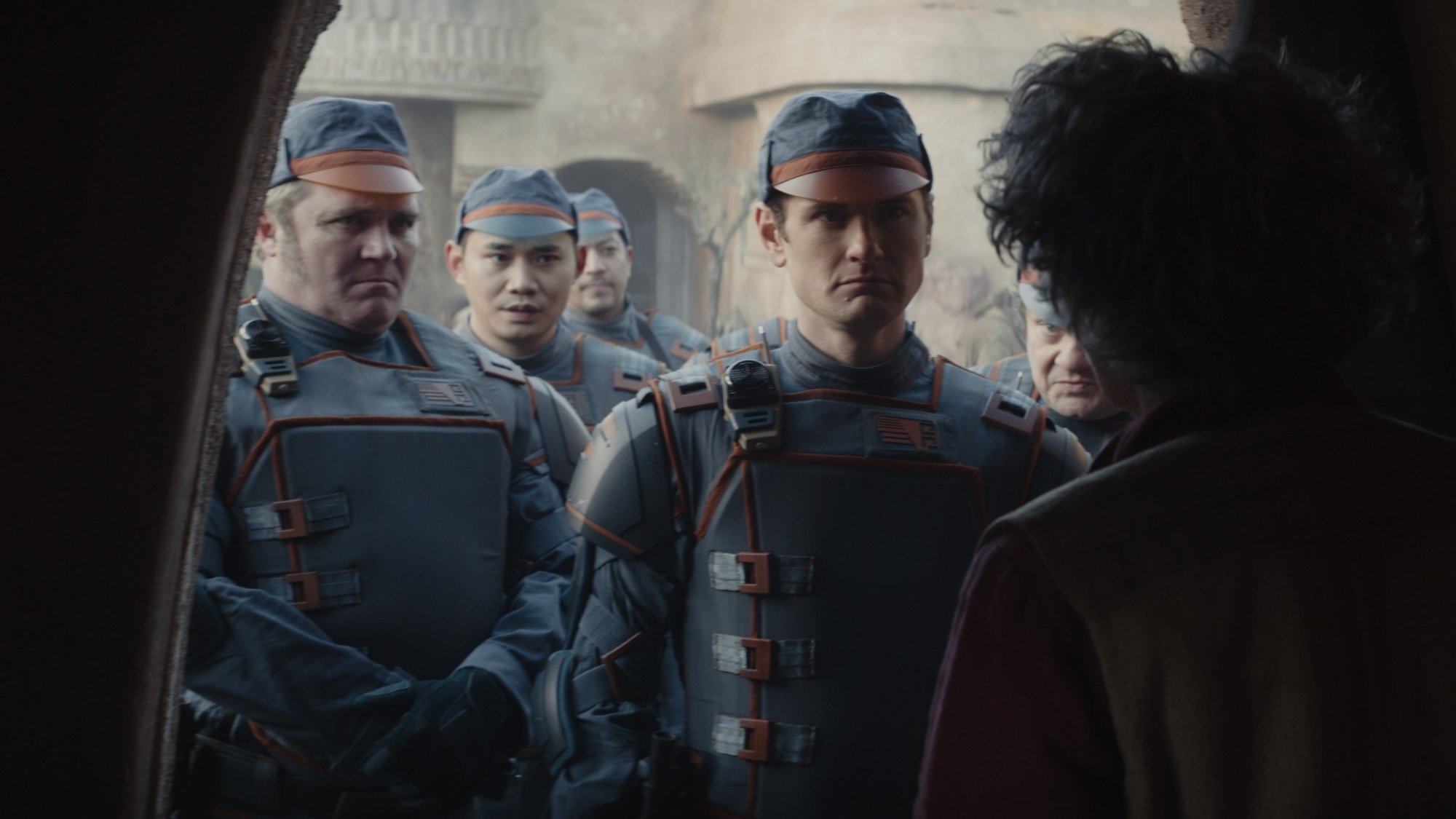 A group of Imperial officers in blue uniforms greet an older woman at the door to her house.