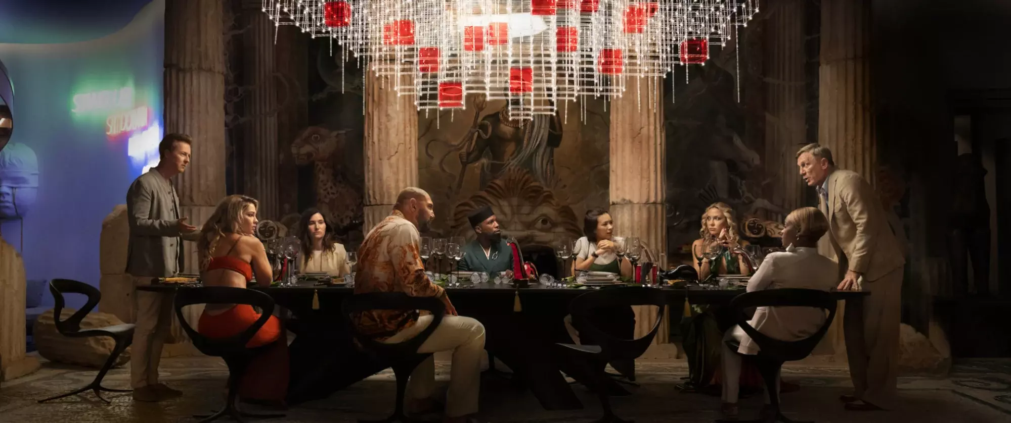 The cast of "Glass Onion" sits around a long table.