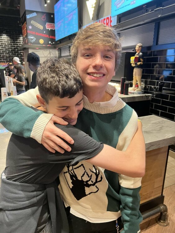 Karl Jacobs smiles as he side hugs a young boy in a gray shirt.