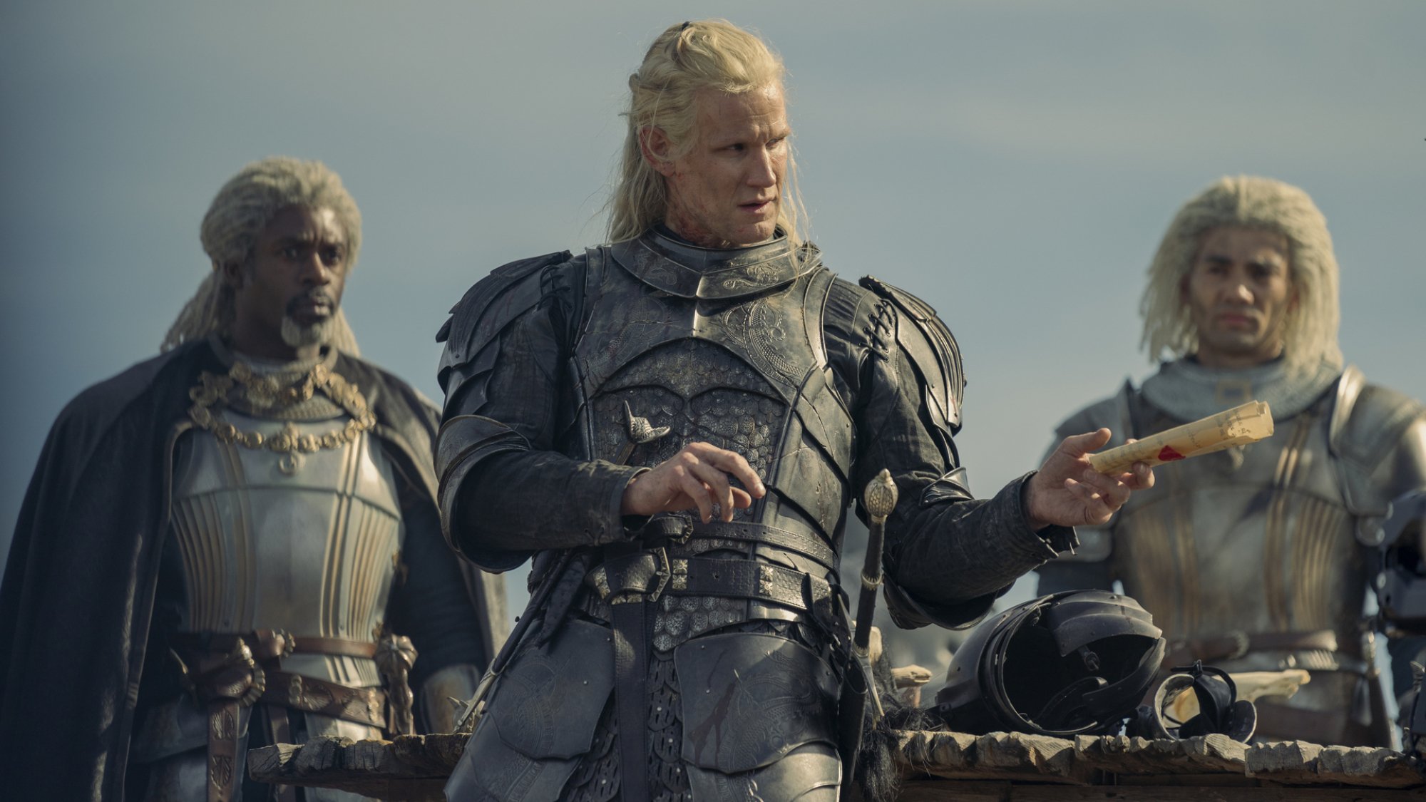 Three men in armor with long braids, one holds a piece of paper.