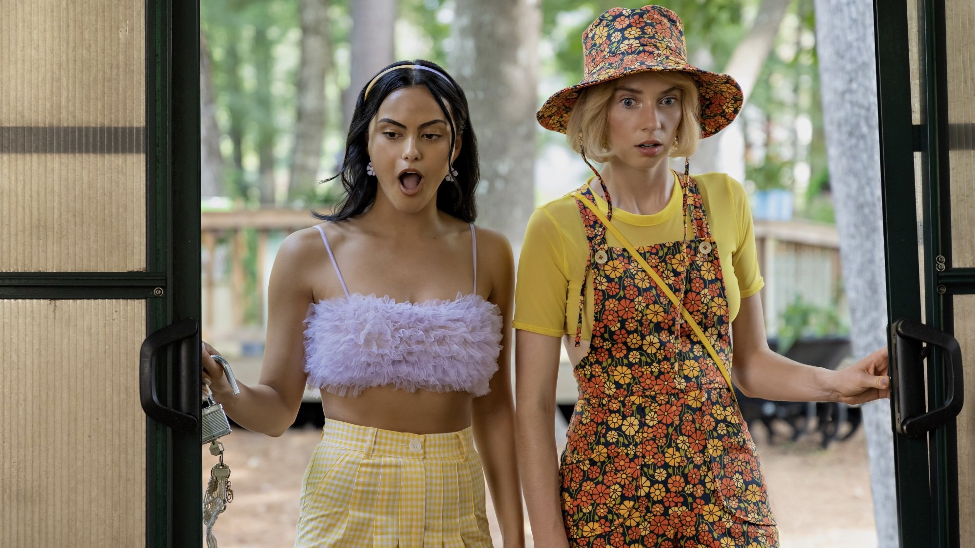 Two young women in colorful outfits look shocked as they enter a greenhouse.
