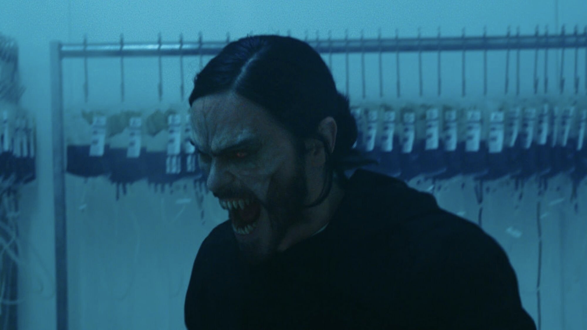 A man with vampire fangs screams in a room full of blood bags.
