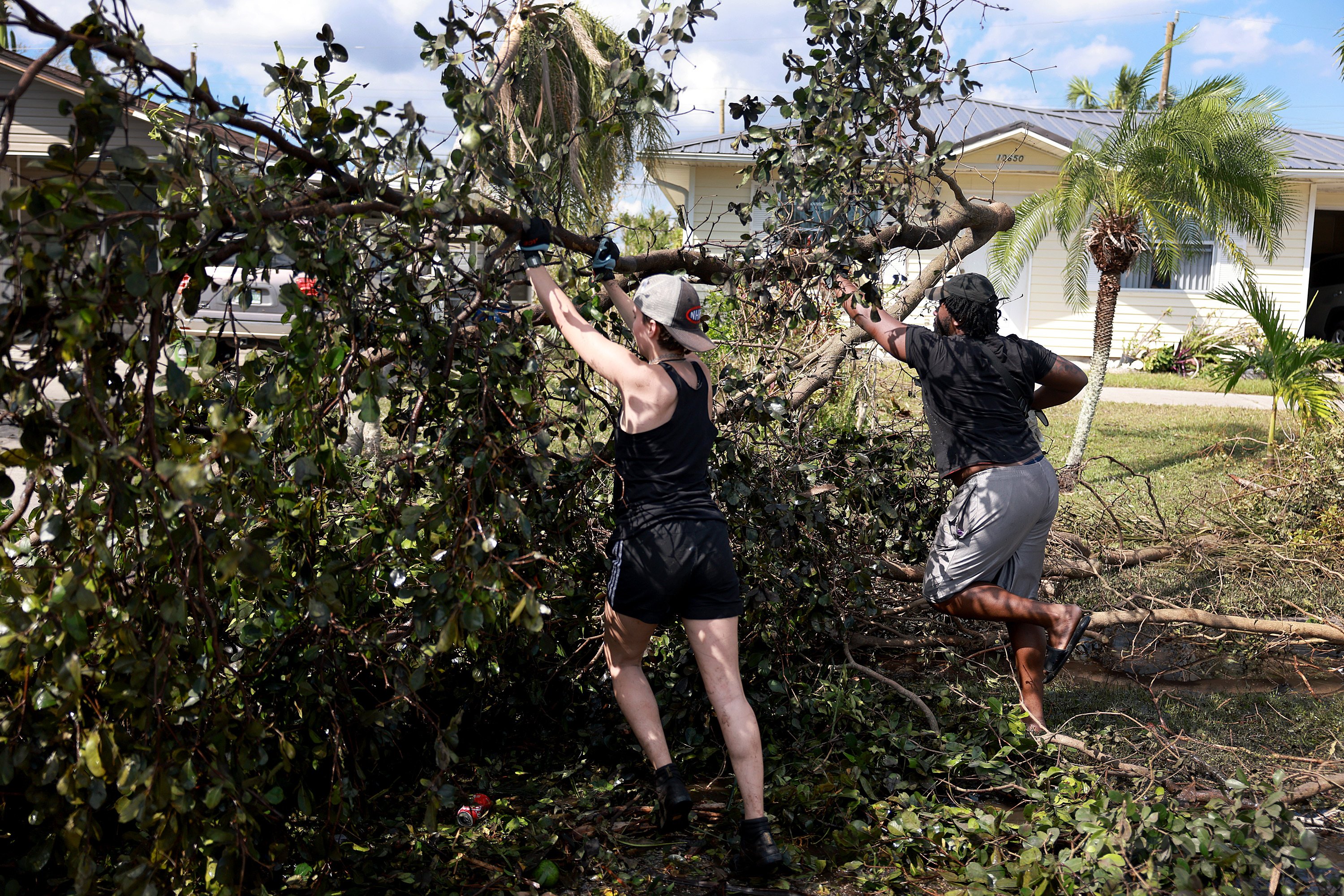 Allison Huston (L) and Malik Jean clear a tree from a road after Hurricane Ian passed through on October 1, 2022 in Fort Myers, Florida. The Category 4 hurricane caused severe damage to the region.