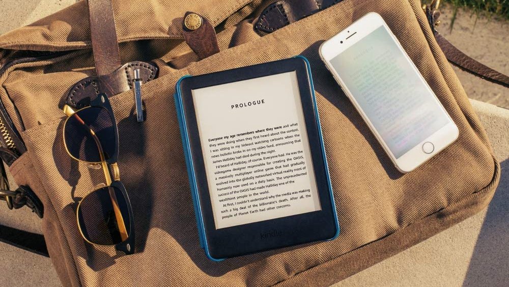 Kindle and iPhone lying on top of canvas bag with glasses hooked onto the front