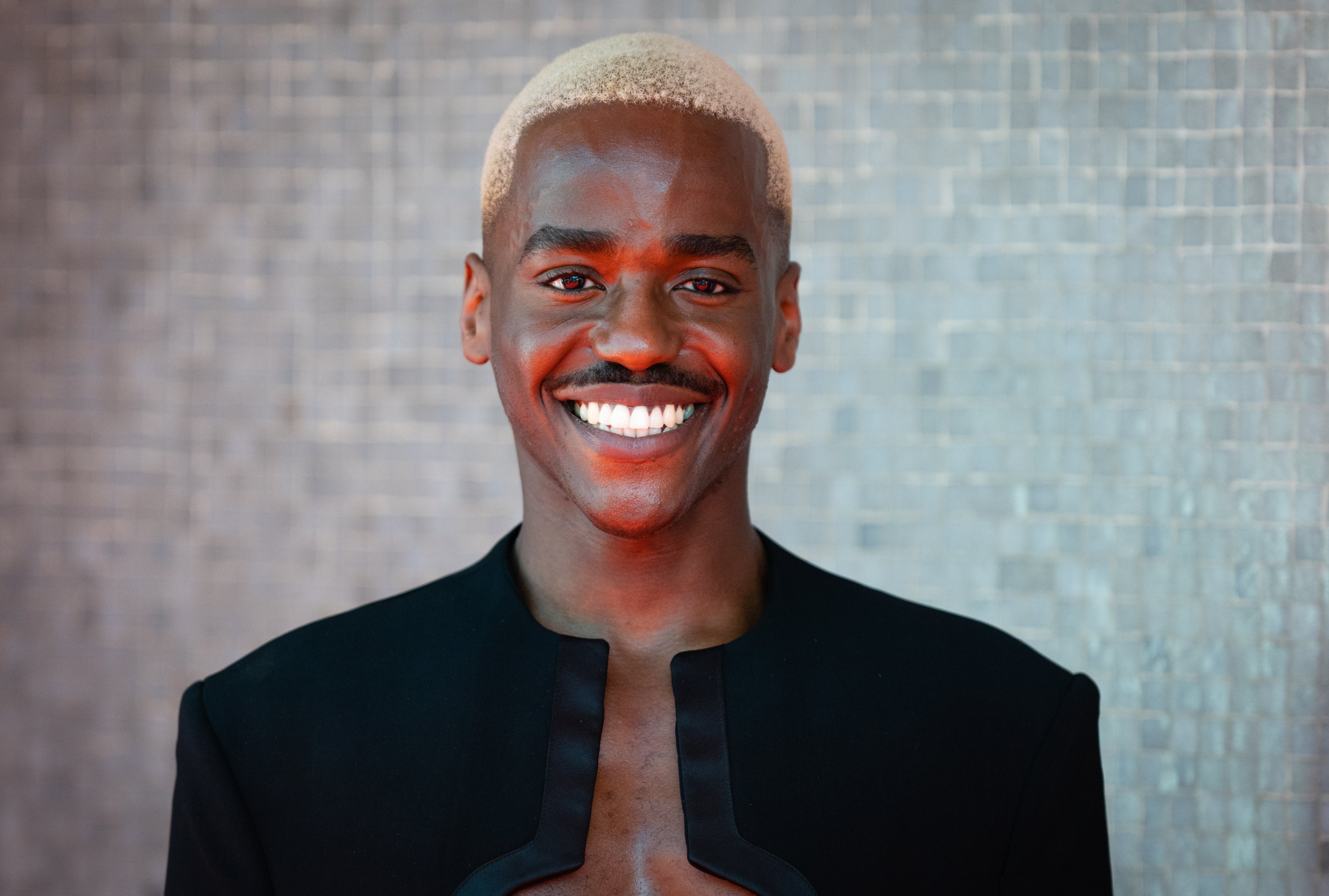 Ncuti Gatwa, a young smiling man with bleached blonde hair and a moustache.
