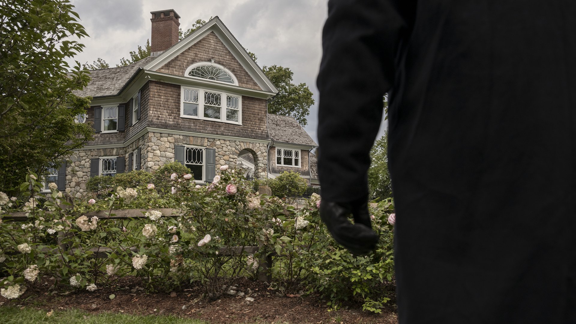 An anonymous person stands staring at a suburban house.