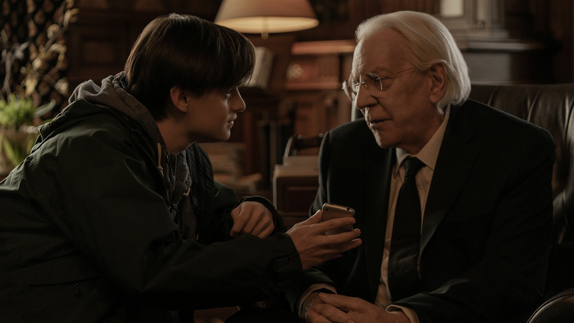 A boy gives a phone to an older man sitting in a chair.