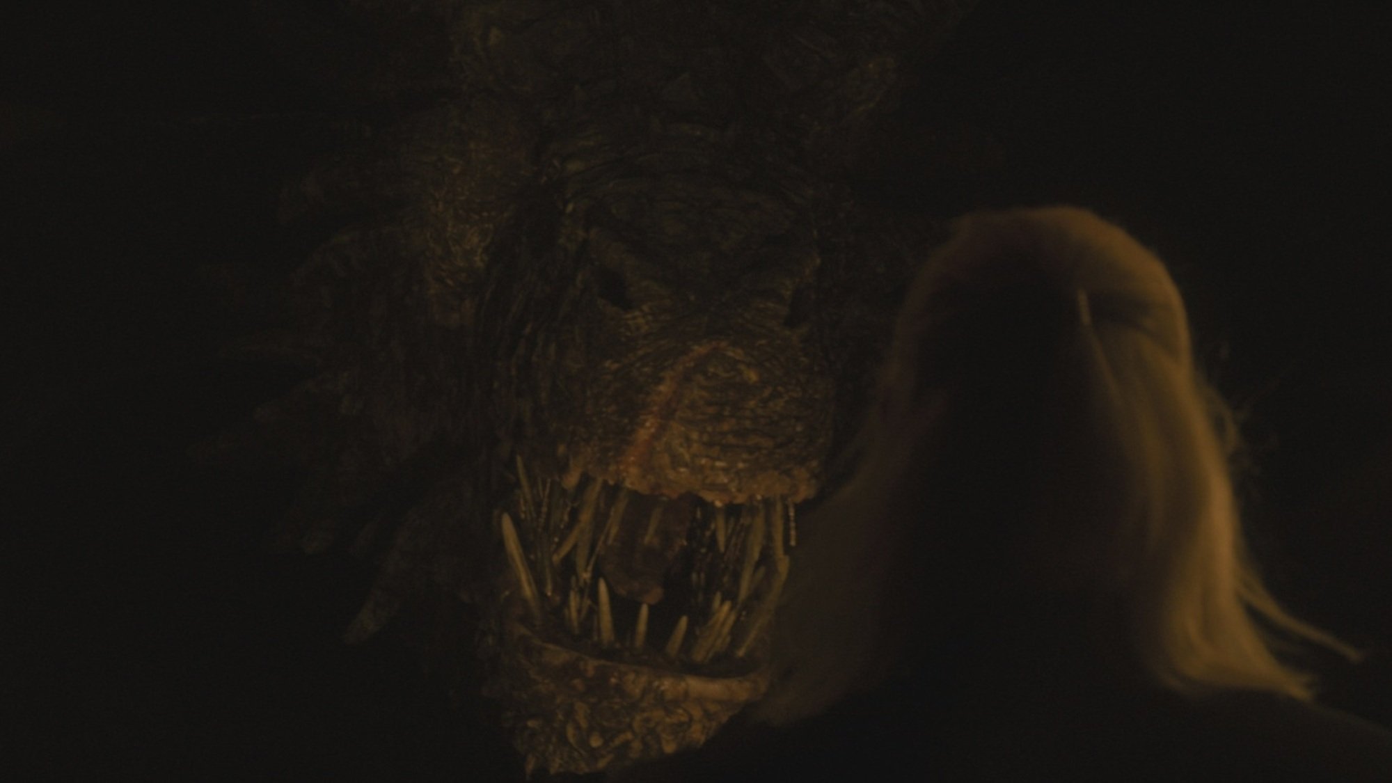 A large bronze dragon stares down at a man with silver blonde hair.