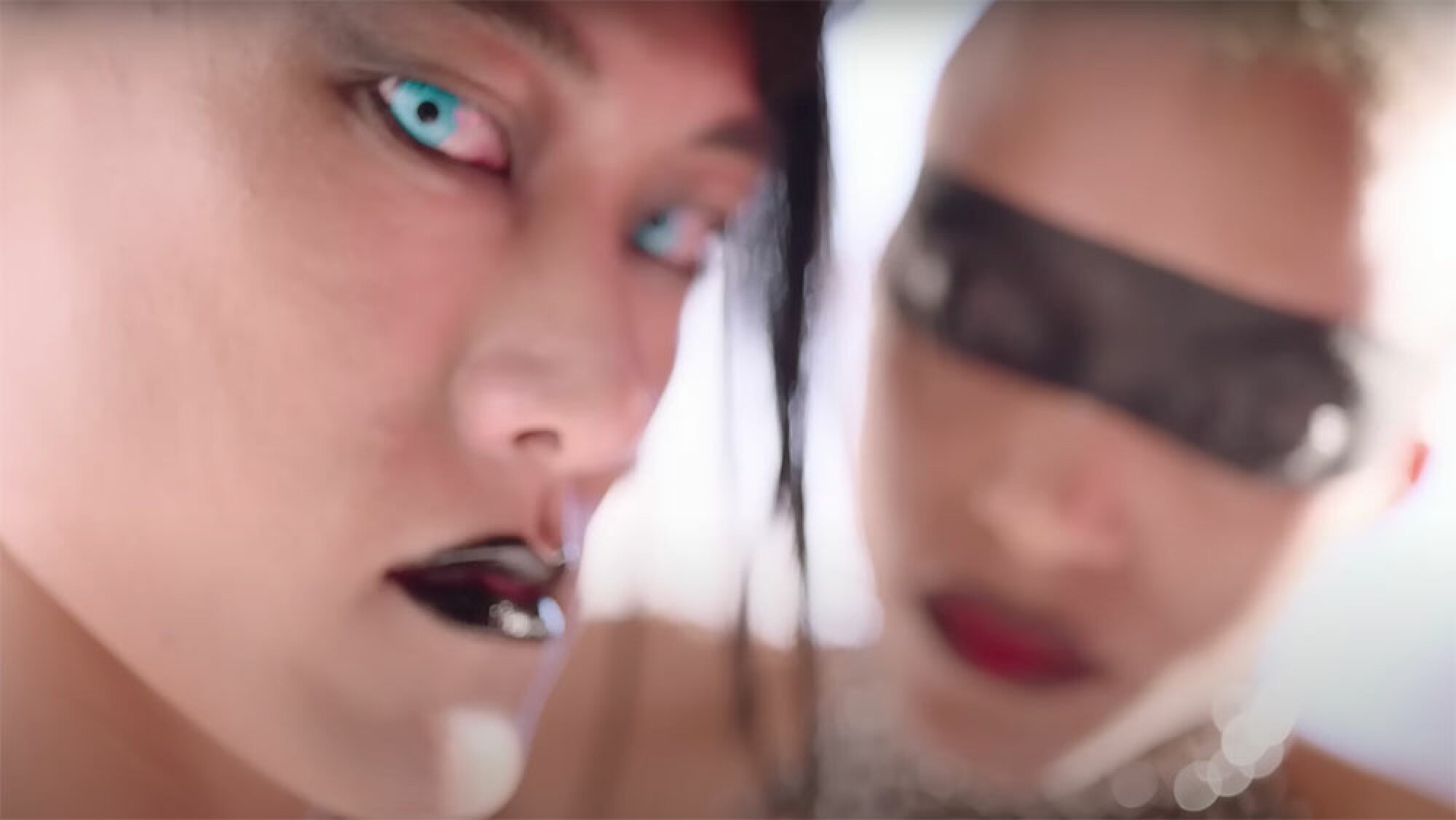Two people wearing makeup turn to look at the camera.
