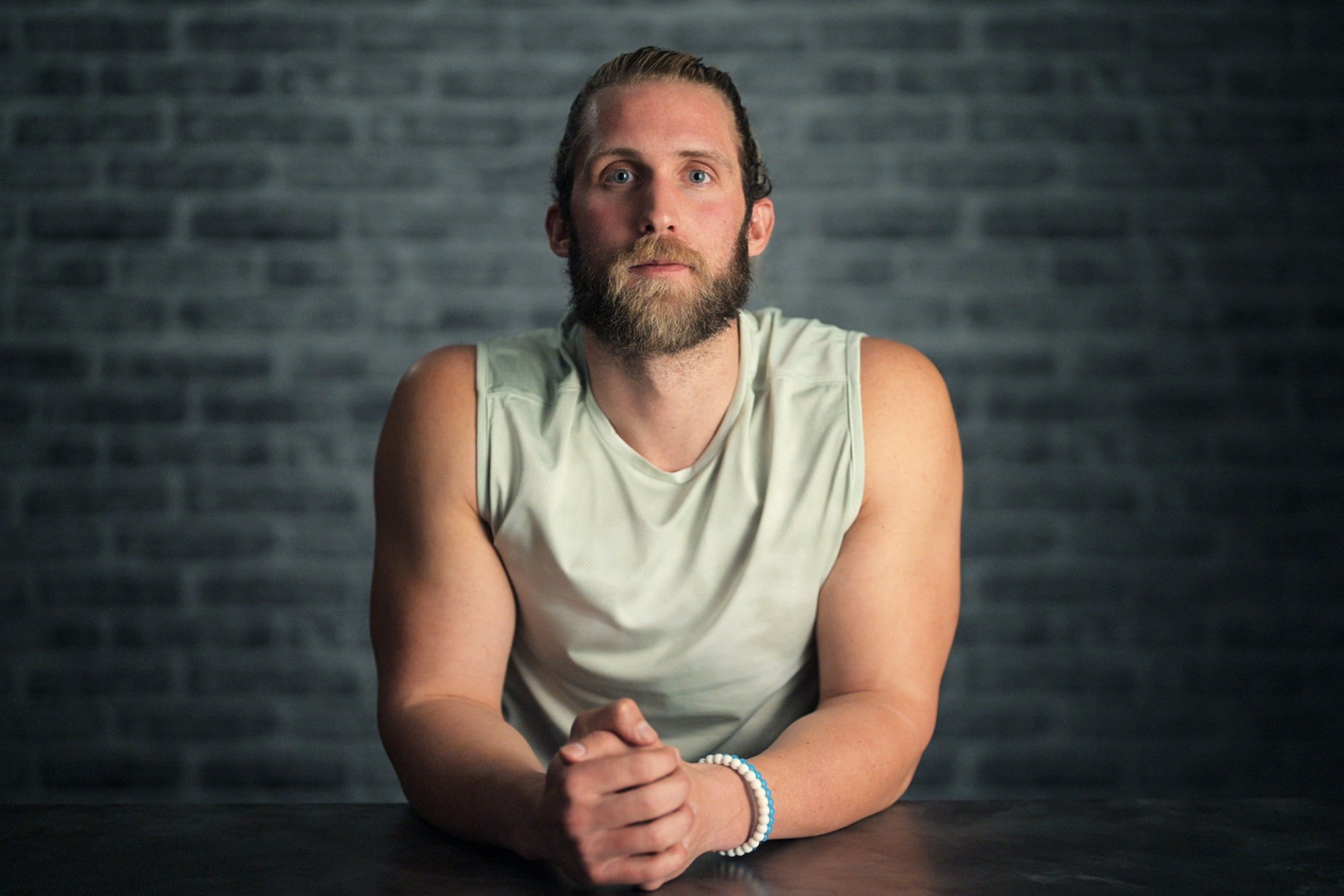 A player on the Netflix series "The Mole" sits facing the camera, a man in a tank top with a beard.