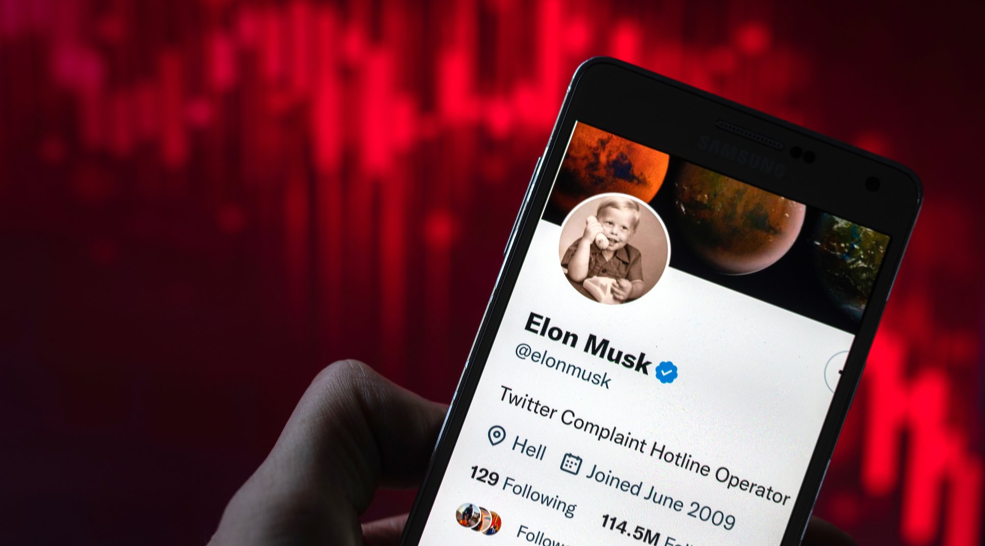 Elon Musk's Twitter handle on a smartphone against a red line declining steeply. 