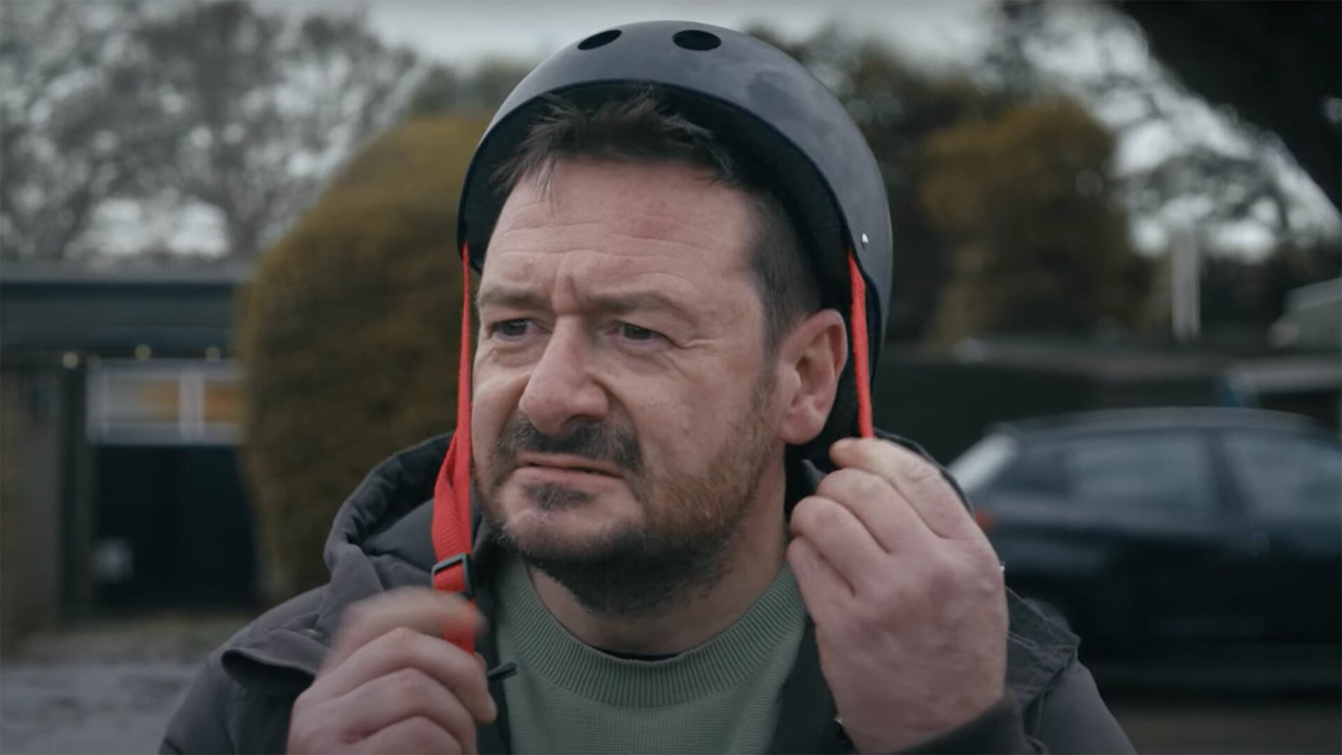 A middle-aged man puts on a skateboard helmet.