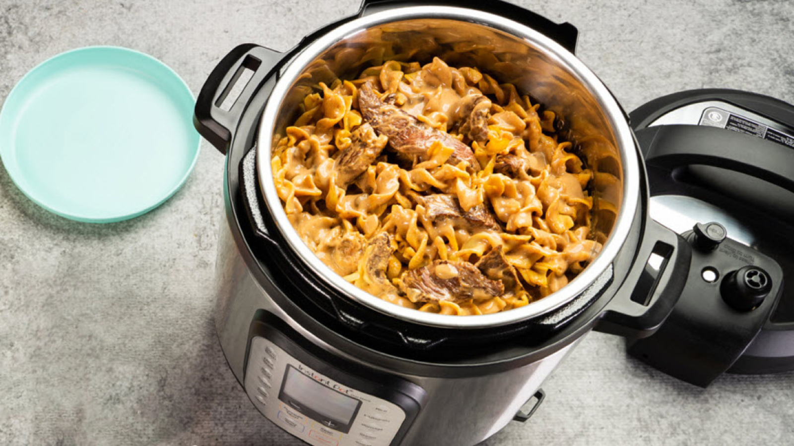 Instant Pot Duo 7-in-1 6-quart multi-cooker containing noodles and meat next to plate on a kitchen counter.