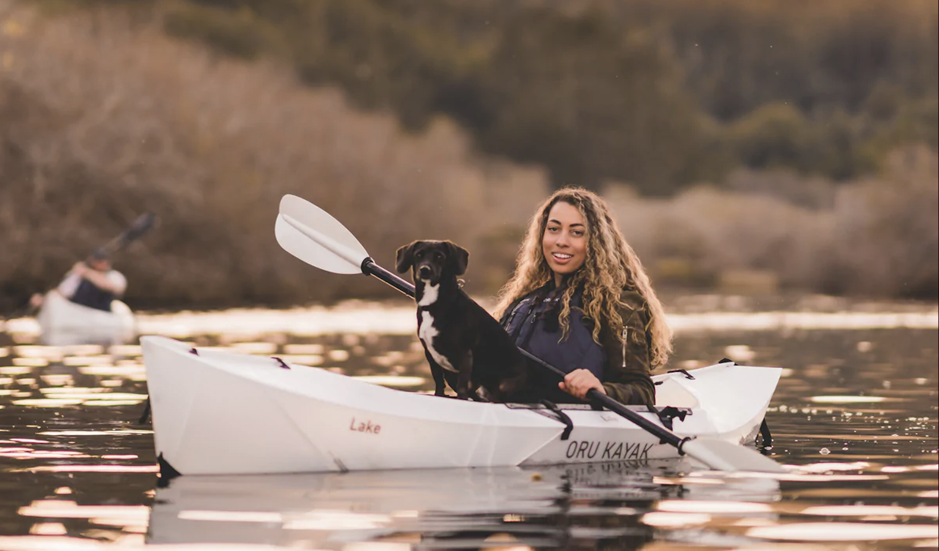 Woman paddling in a white kayak with a black dog
