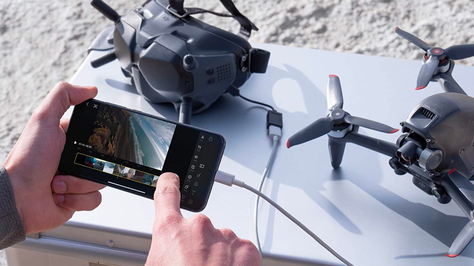 a close-up of a person looking at drone footage on a smartphone in front of a dji drone and its goggles sitting on a metal case
