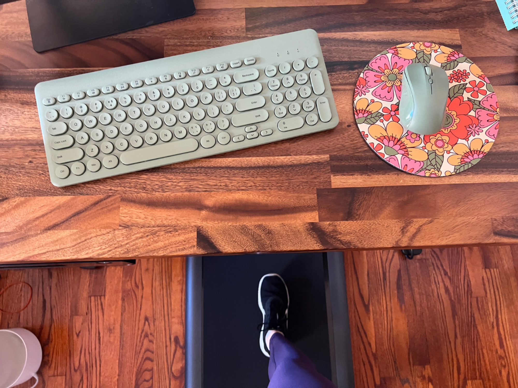 keyboard and mouse on desktop with feet walking on treadmill in background
