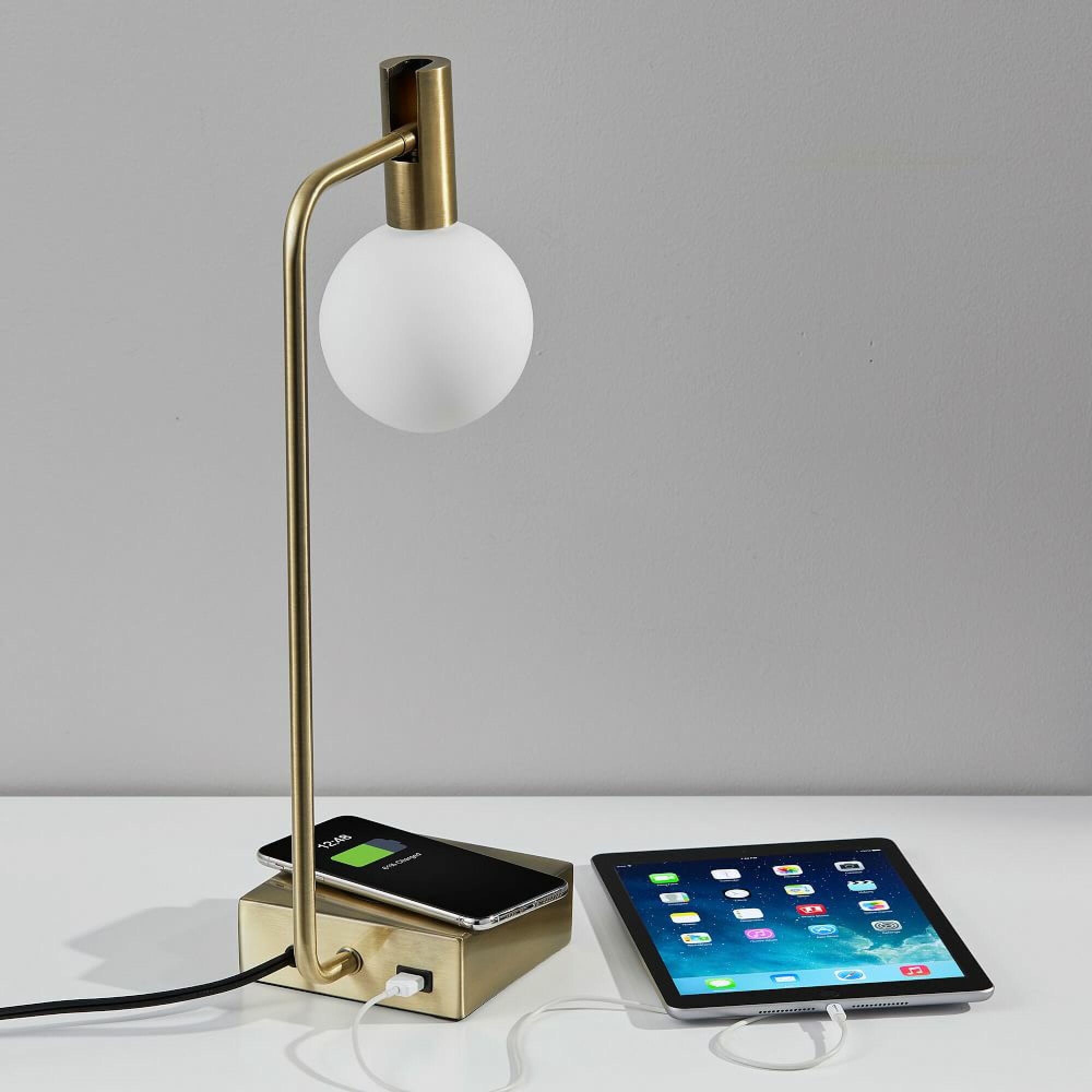 West Elm brass lamp with a smartphone charging on its base and an ipad plugged into its USB port.