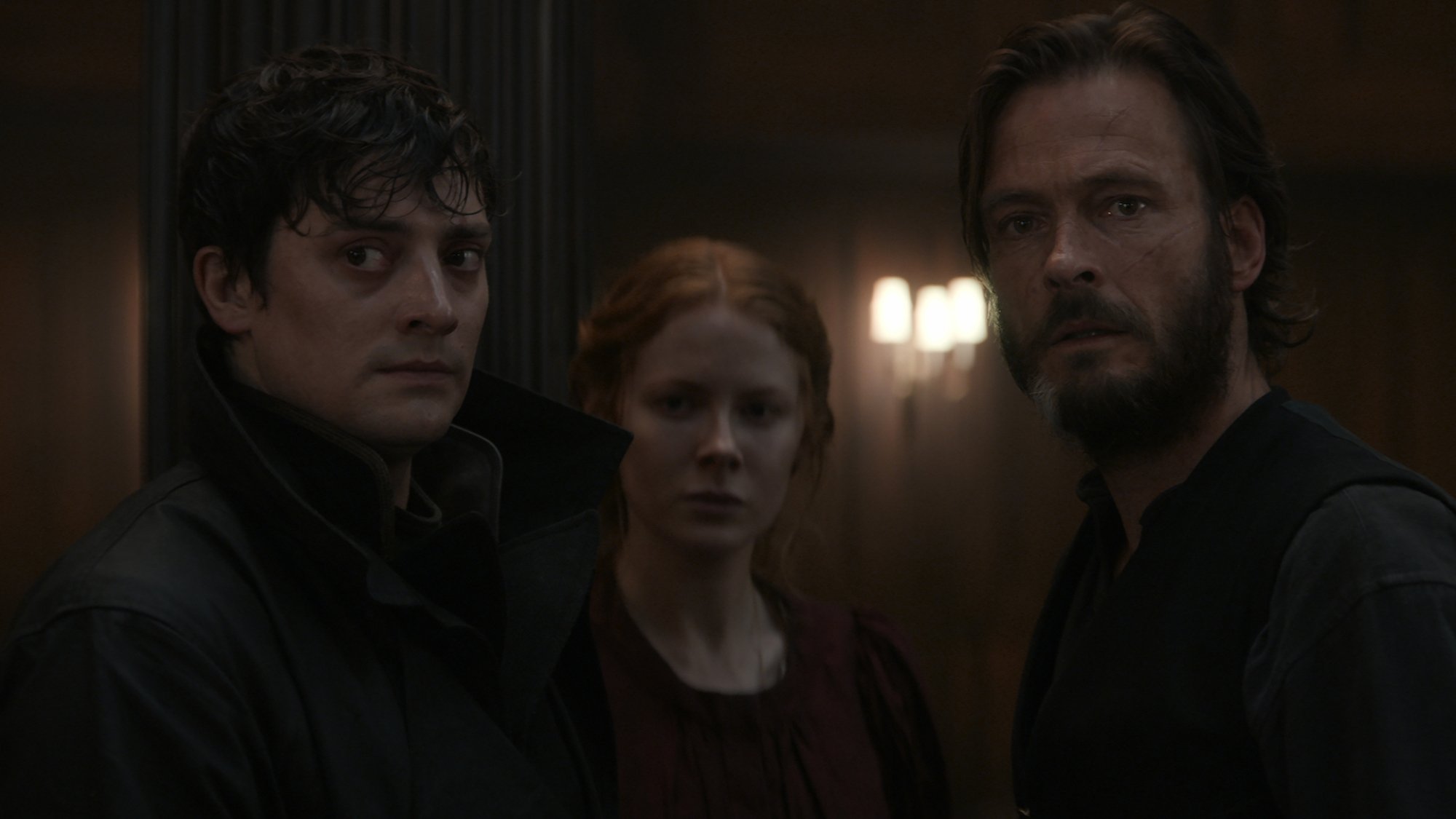 Three people stand in a dark wood-panelled room looking stressed.