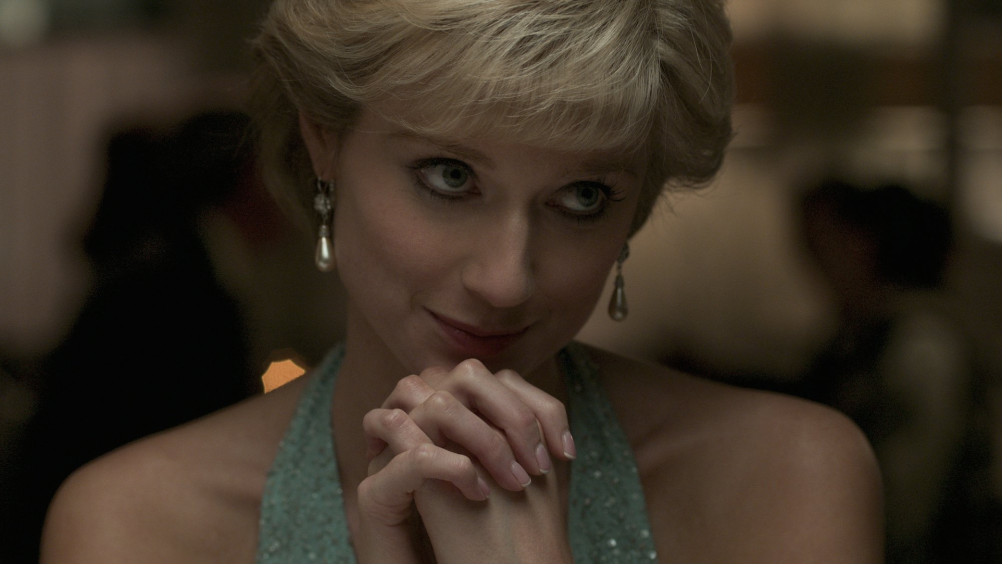 A woman in a light blue halter evening gown clasps her hands and smiles.