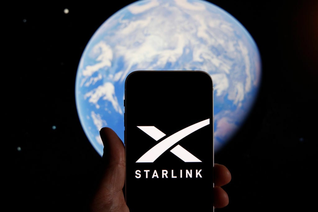 The Starlink logo on a smartphone, in front of an image of the Earth from space.