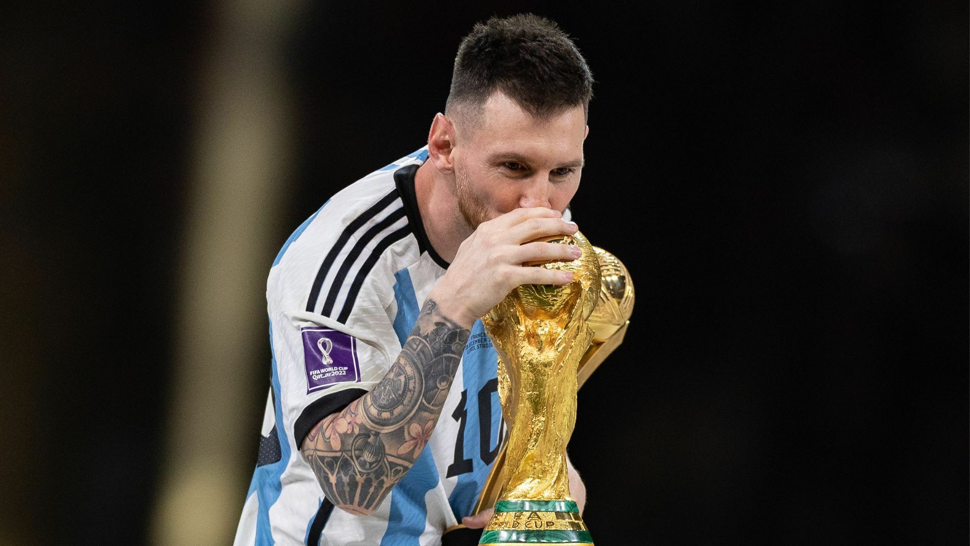 A footballer wearing an Argentina uniform kisses the World Cup trophy.