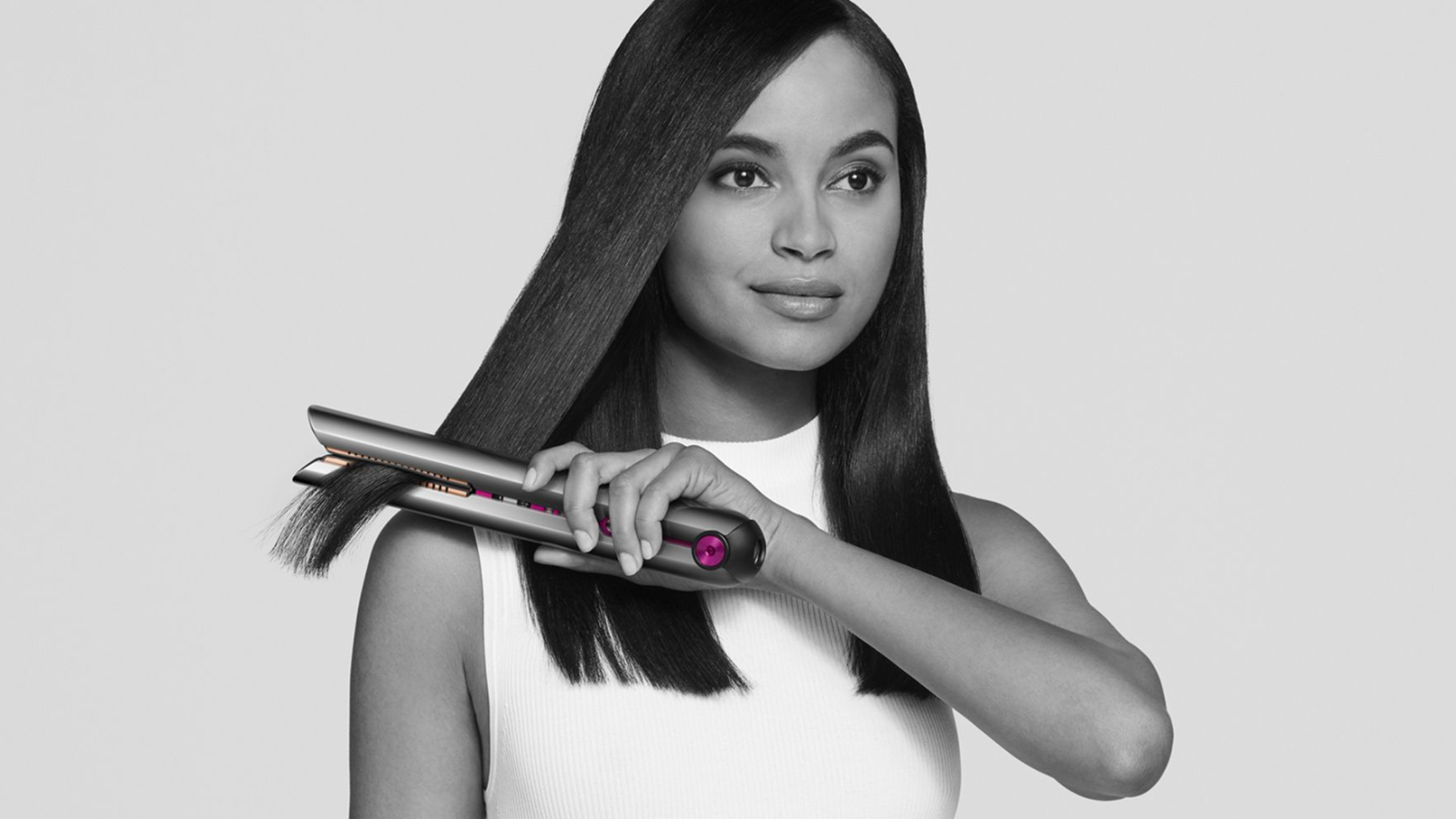 a black and white image of a woman in a white shirt straightening her hair with a dyson corrale