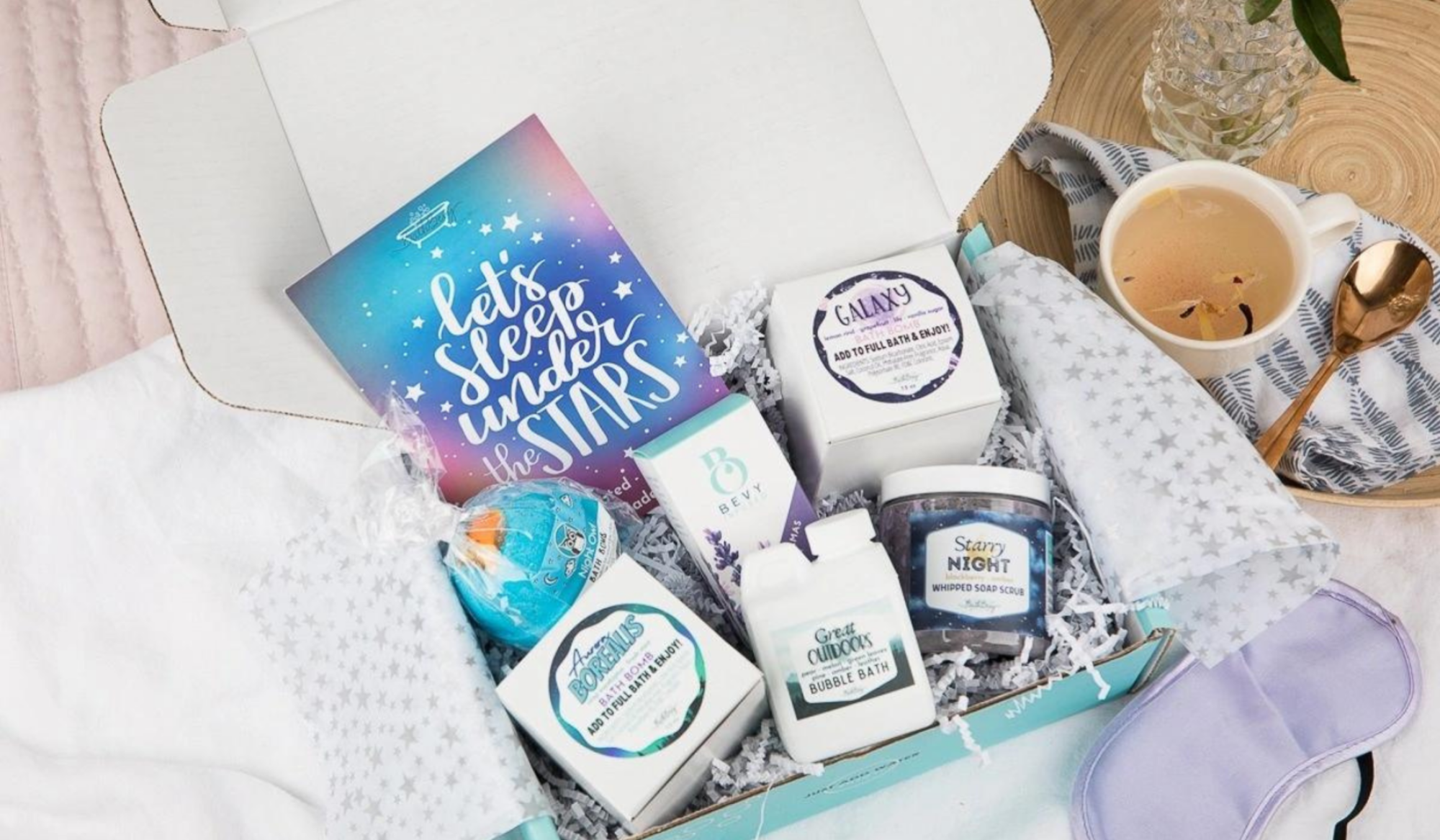 Box of themed bath items on bed with cup of coffee in corner