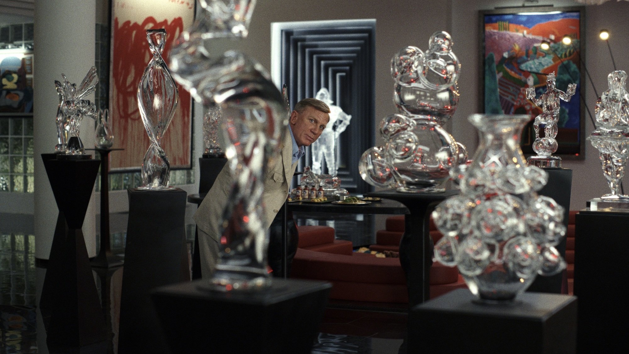 A man in a suit walks through a gallery of glass sculptures on pedestals.