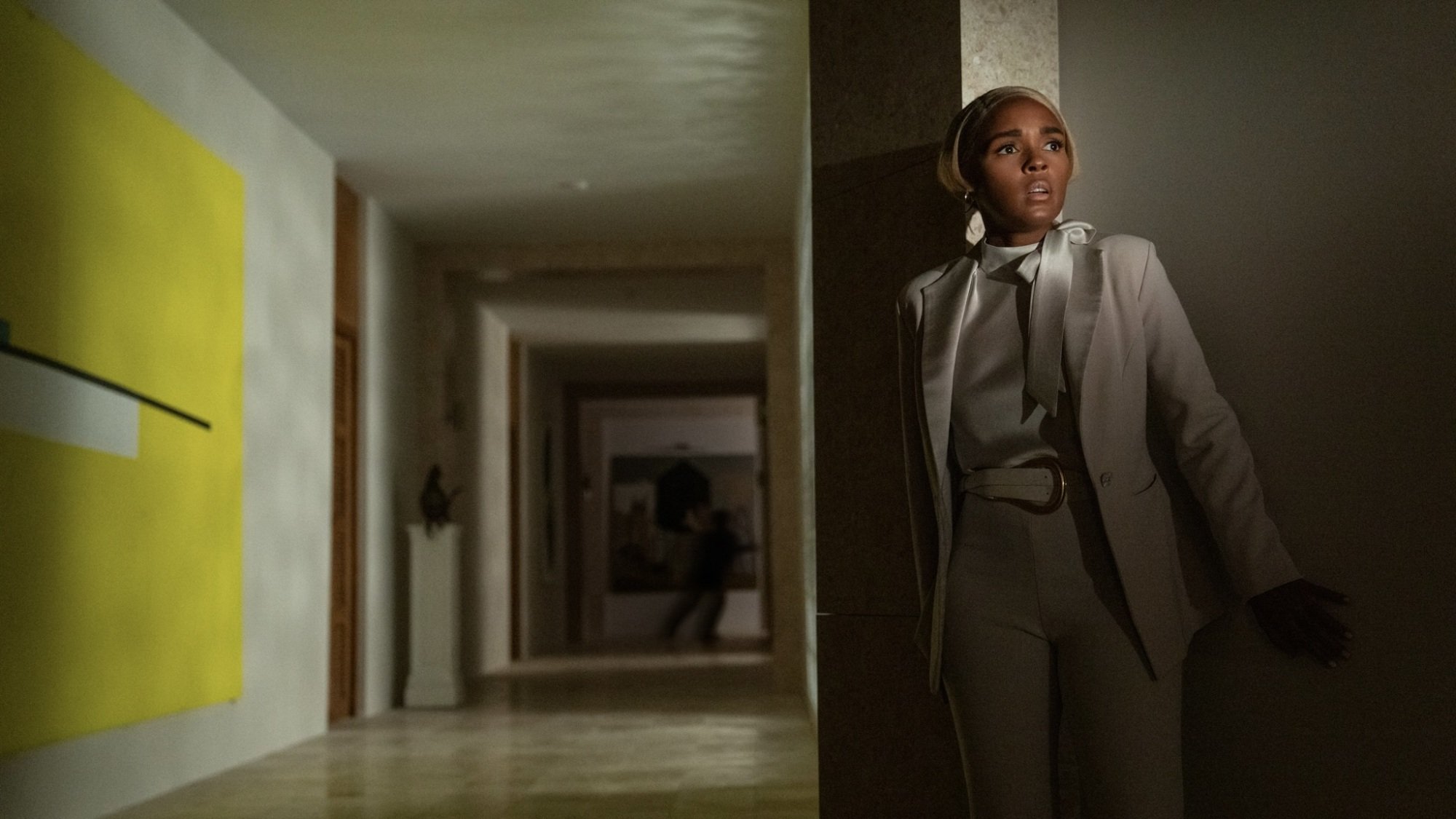 A woman in a white suit hides behind a corner, looking frightened.