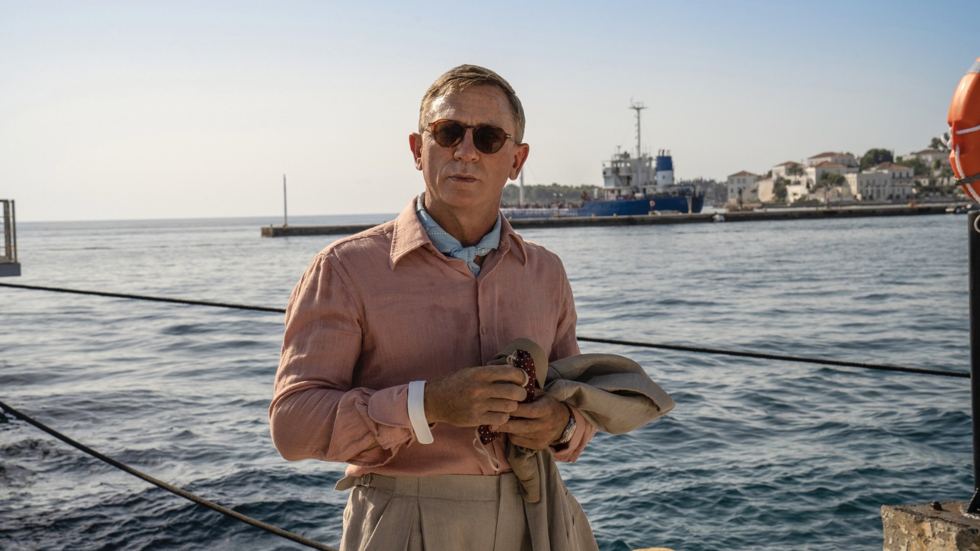 A man in a pink shirt stands on a dock overlooking the ocean.