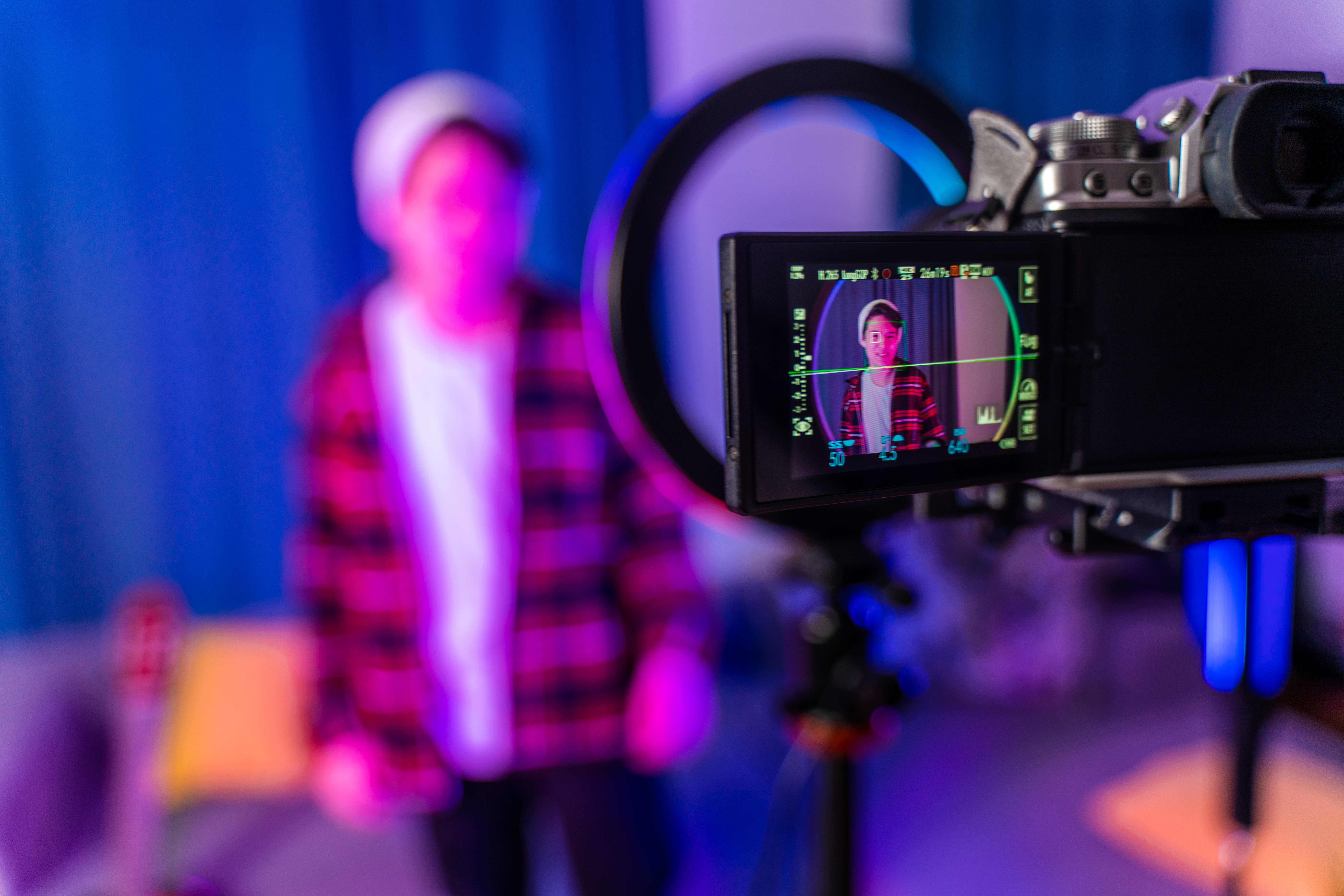 A young teenager stands in a colorful room in front of camera and artificial light.