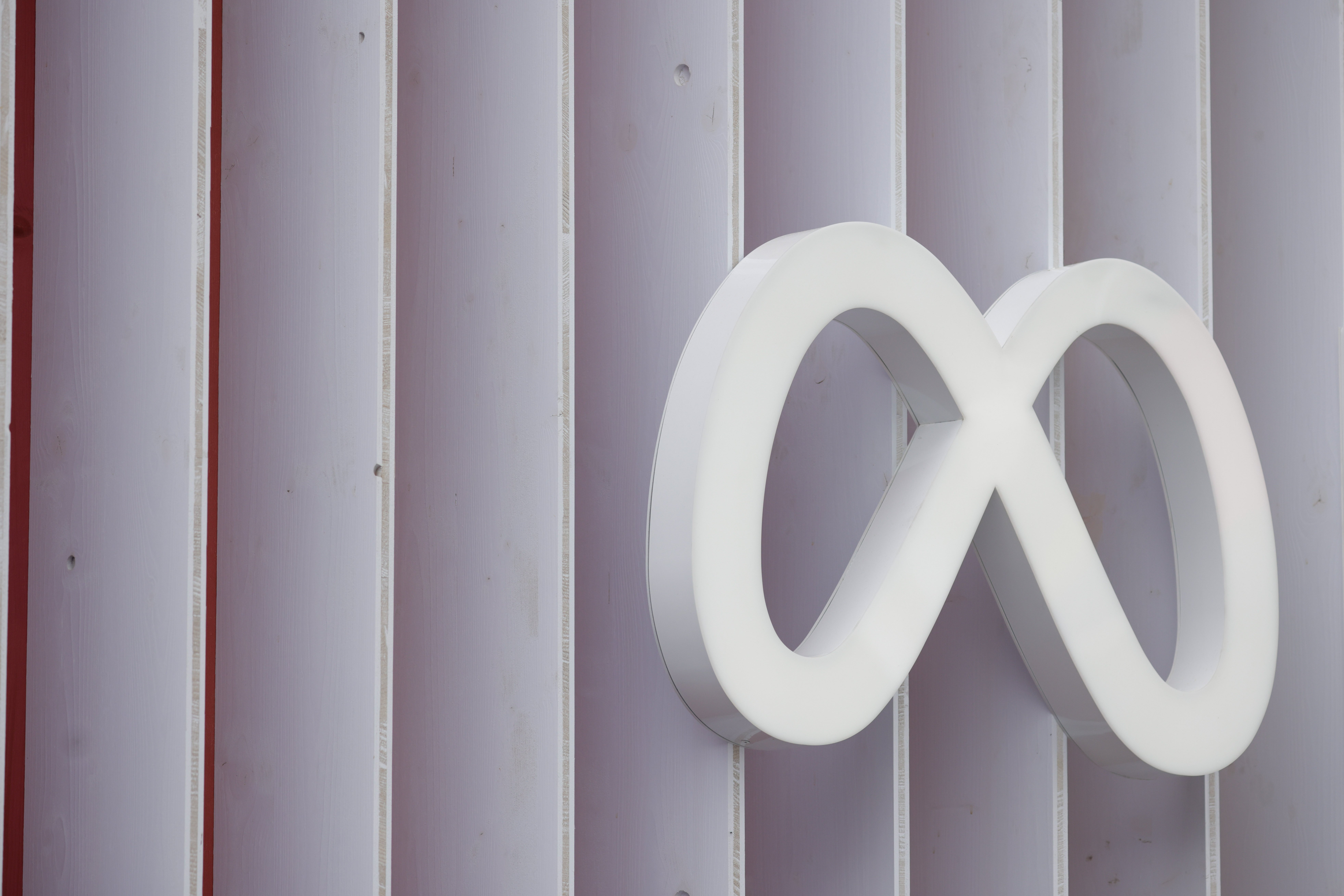 A white Meta logo sign on a white-paneled wall.