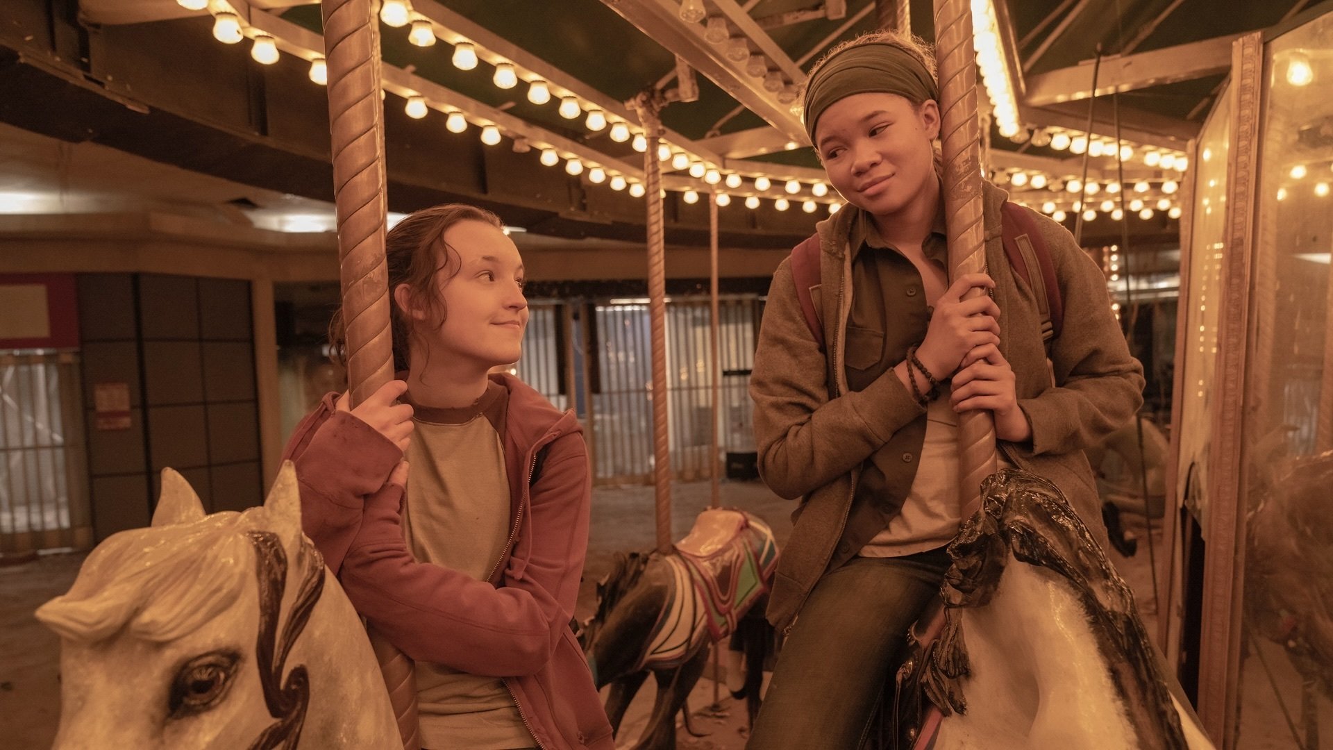 Two teenage girls ride an indoor carousel together.