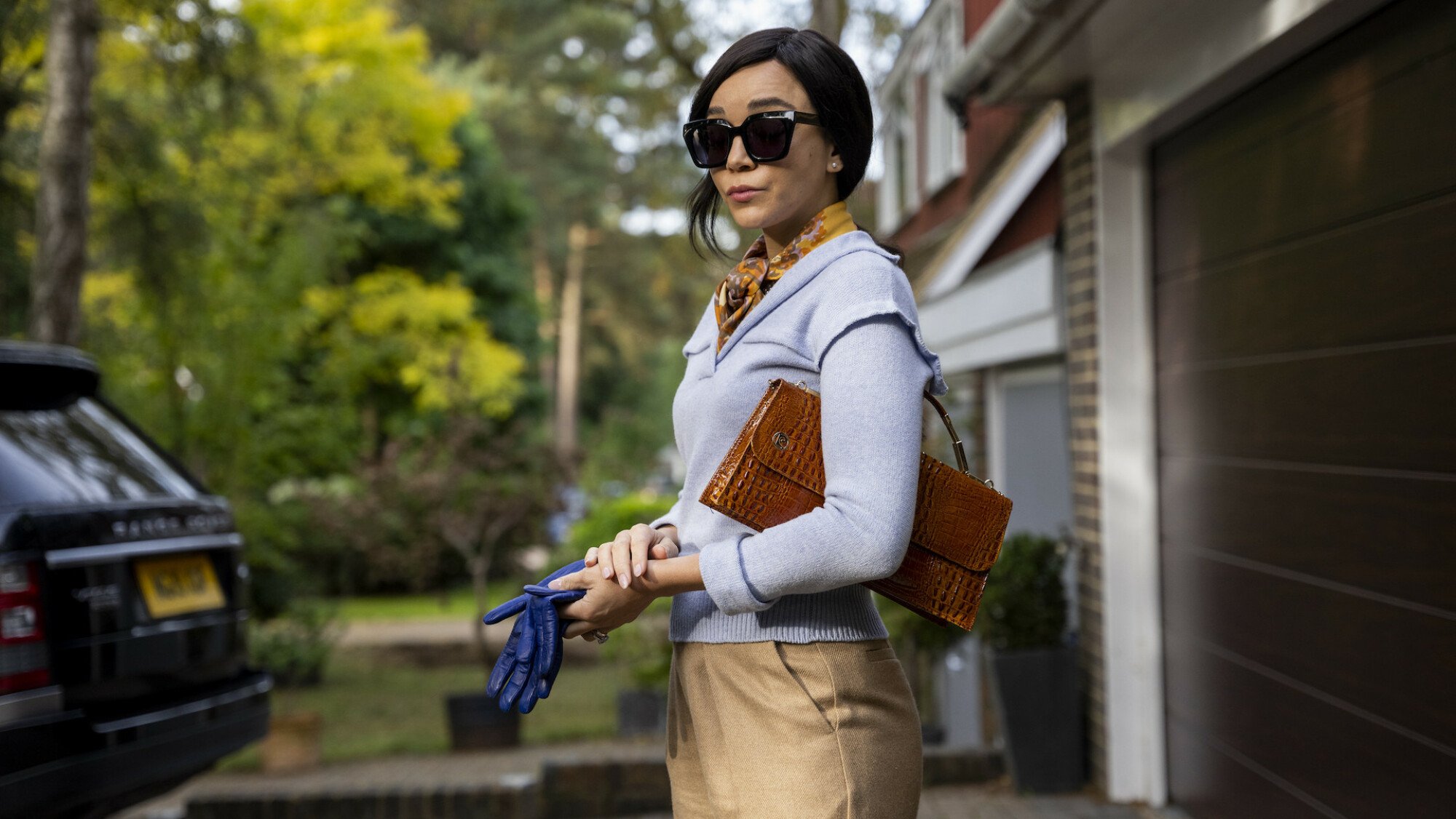 A fashionable woman stands in her driveway in an affluent neighbourhood.