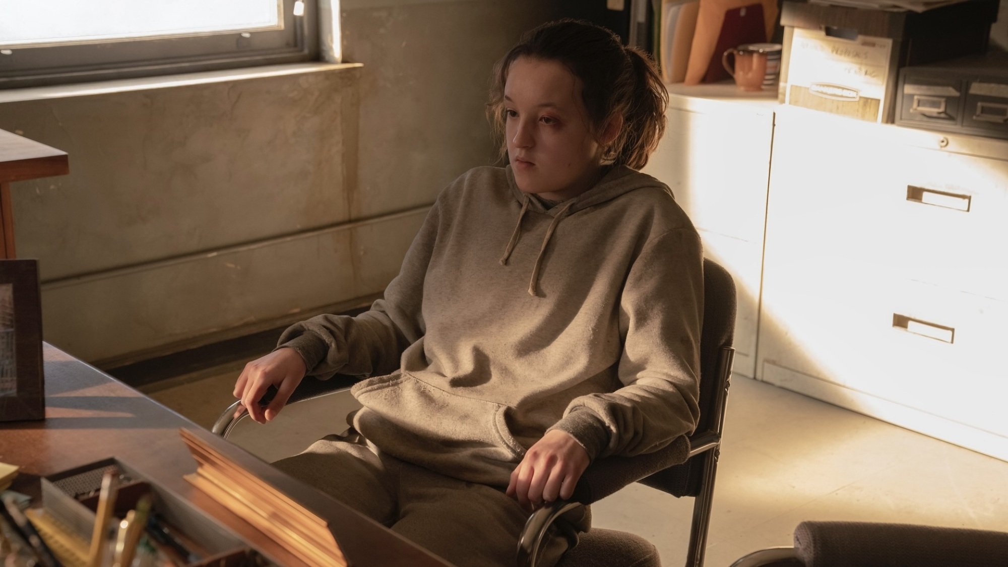 A teenage girl in a grey sweatshirt sits in front of a desk.