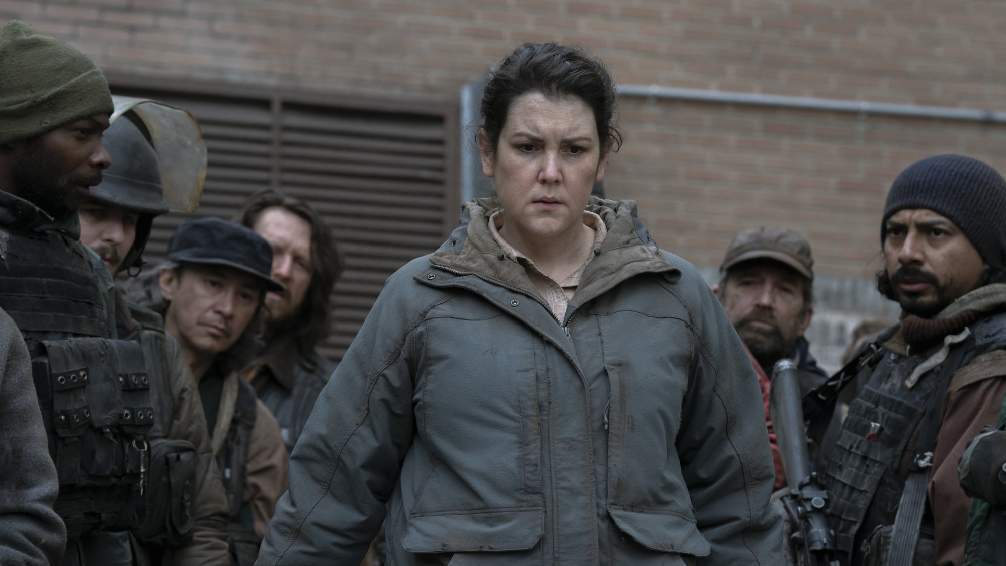 A woman looks down at something troubling, surrounded by soldiers.