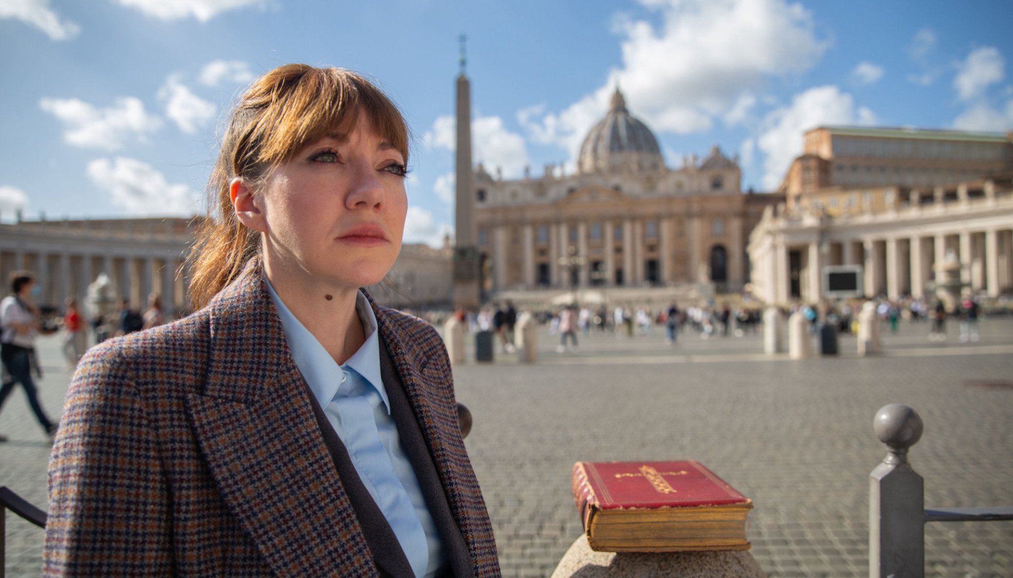 A woman in a suit stands outside St Peters Basilica, looking upward.