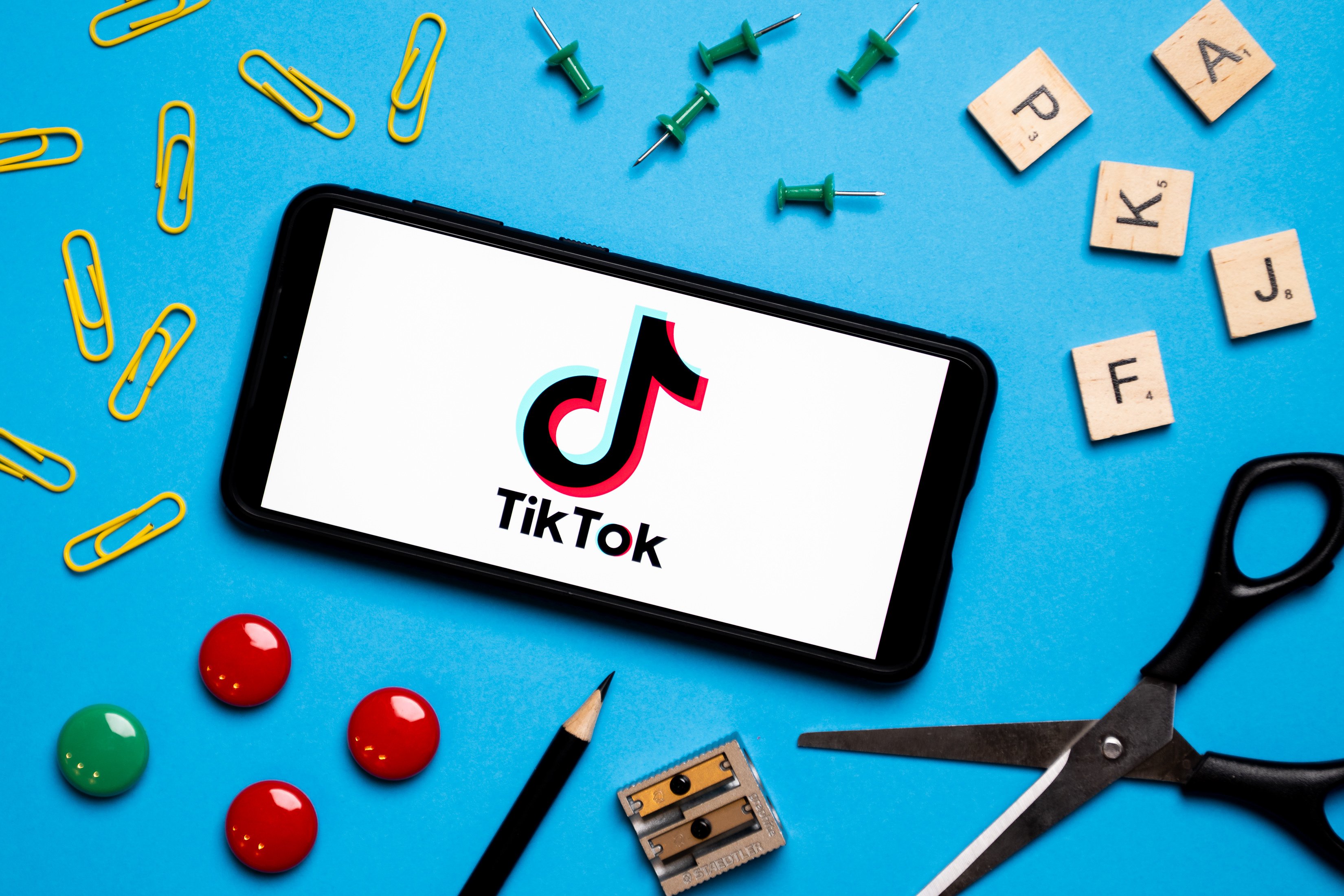 A phone with the TikTok logo on a light blue background surrounded by school supplies. 