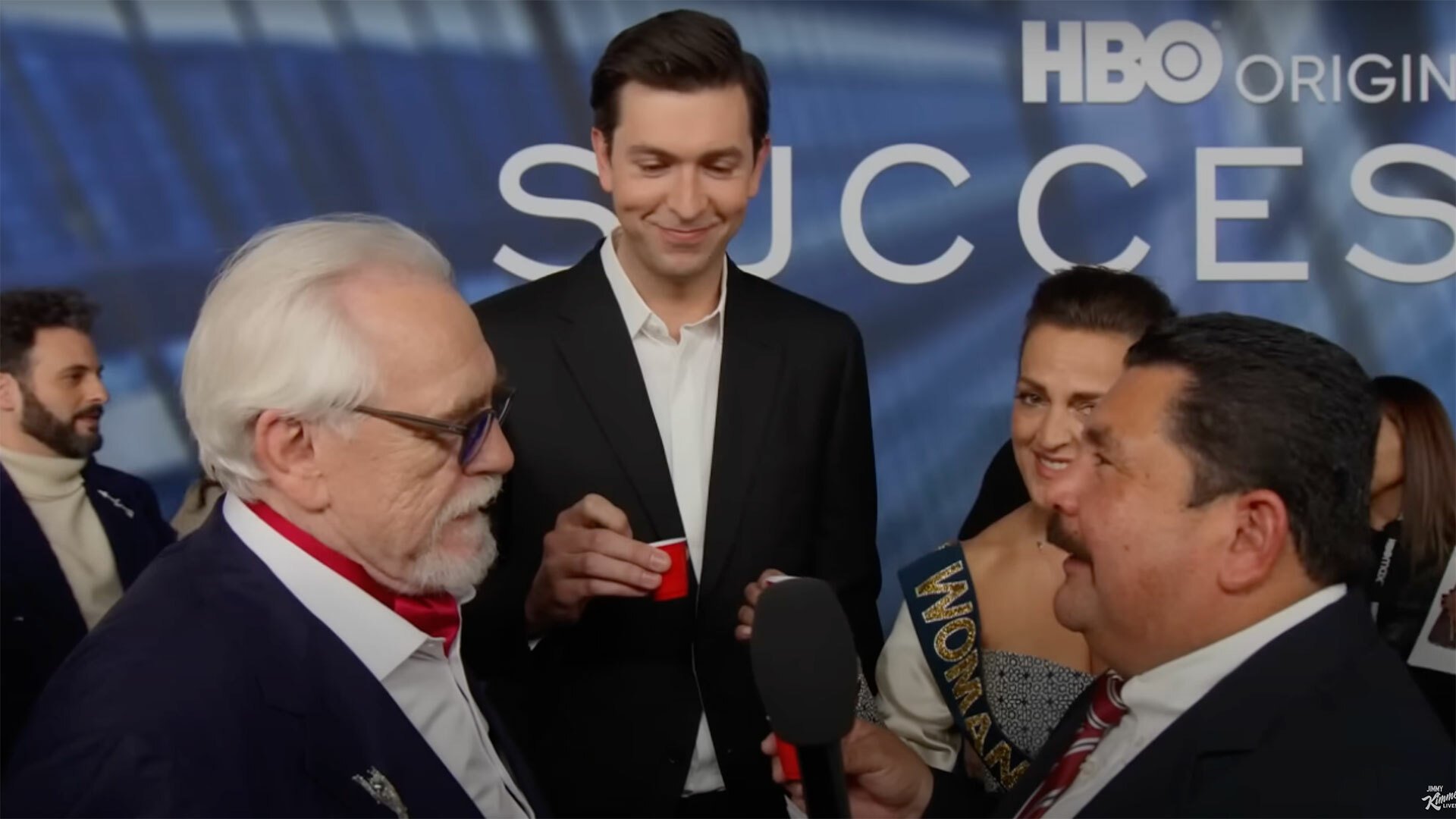 A group of people at a premiere raise red shot glasses.