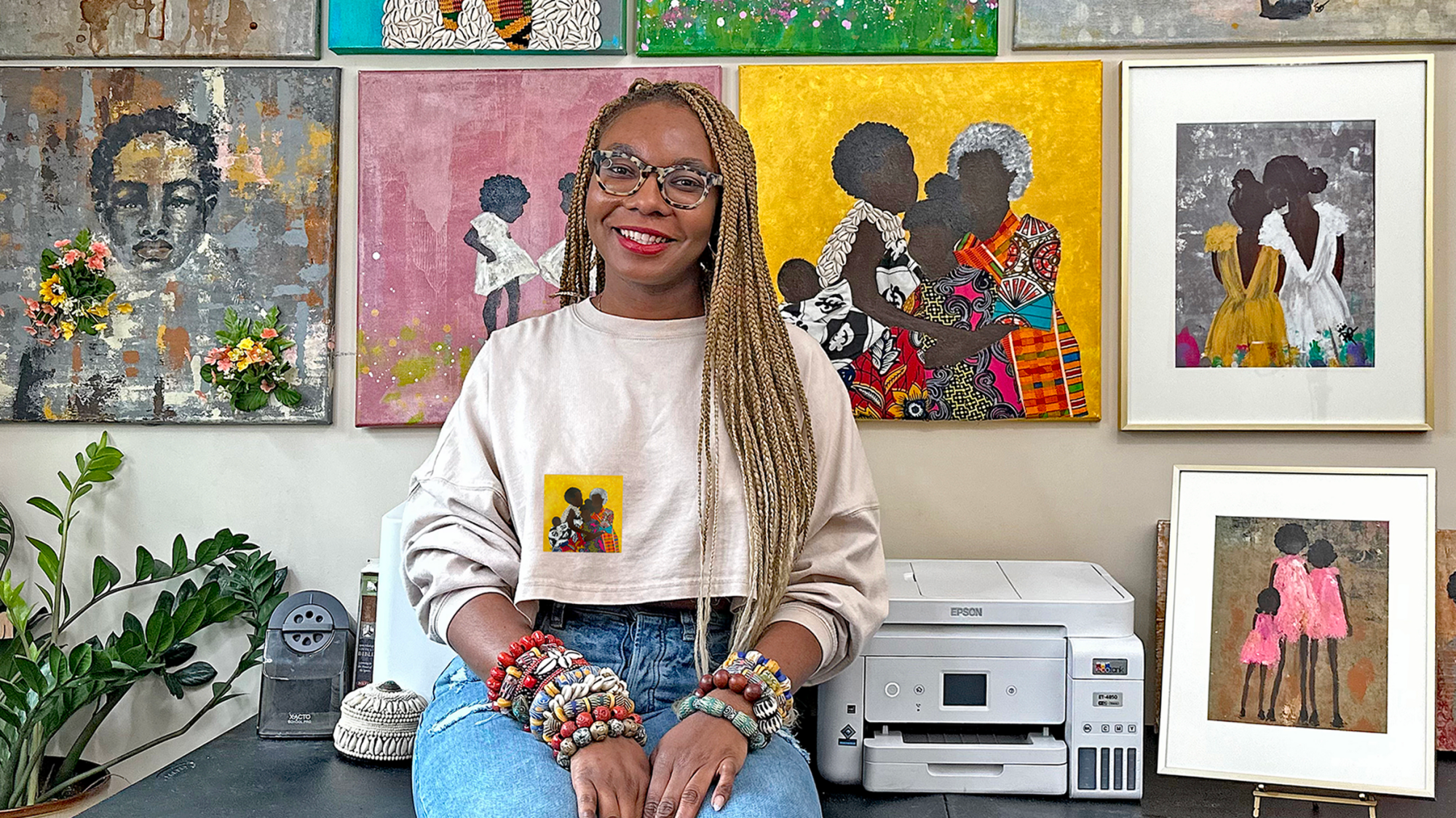 Racquèl Dwomoh sitting in front of her artwork