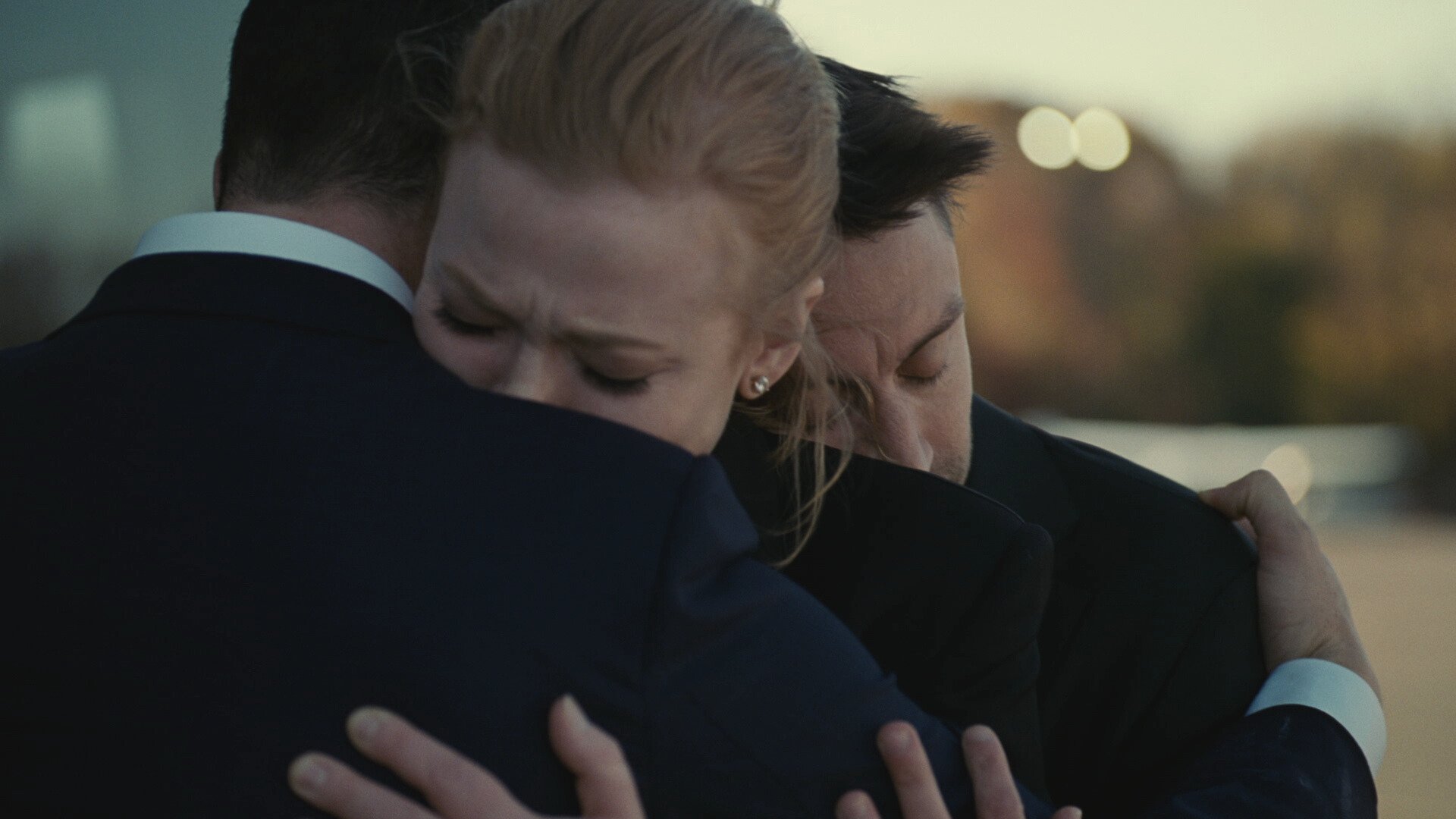 Two men and a woman group hug while crying.