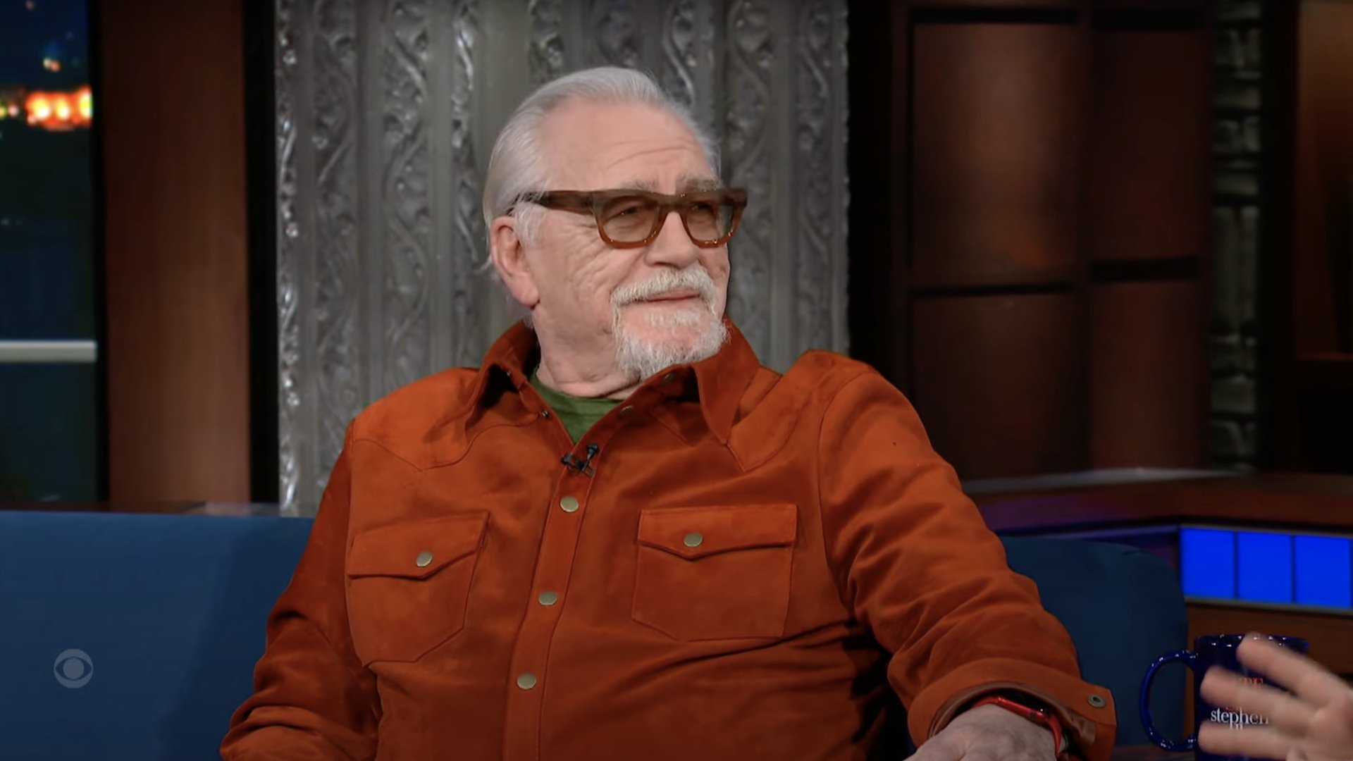 Actor Brian Cox appears on The Late Show wearing dark glasses and a bright red/orange shirt