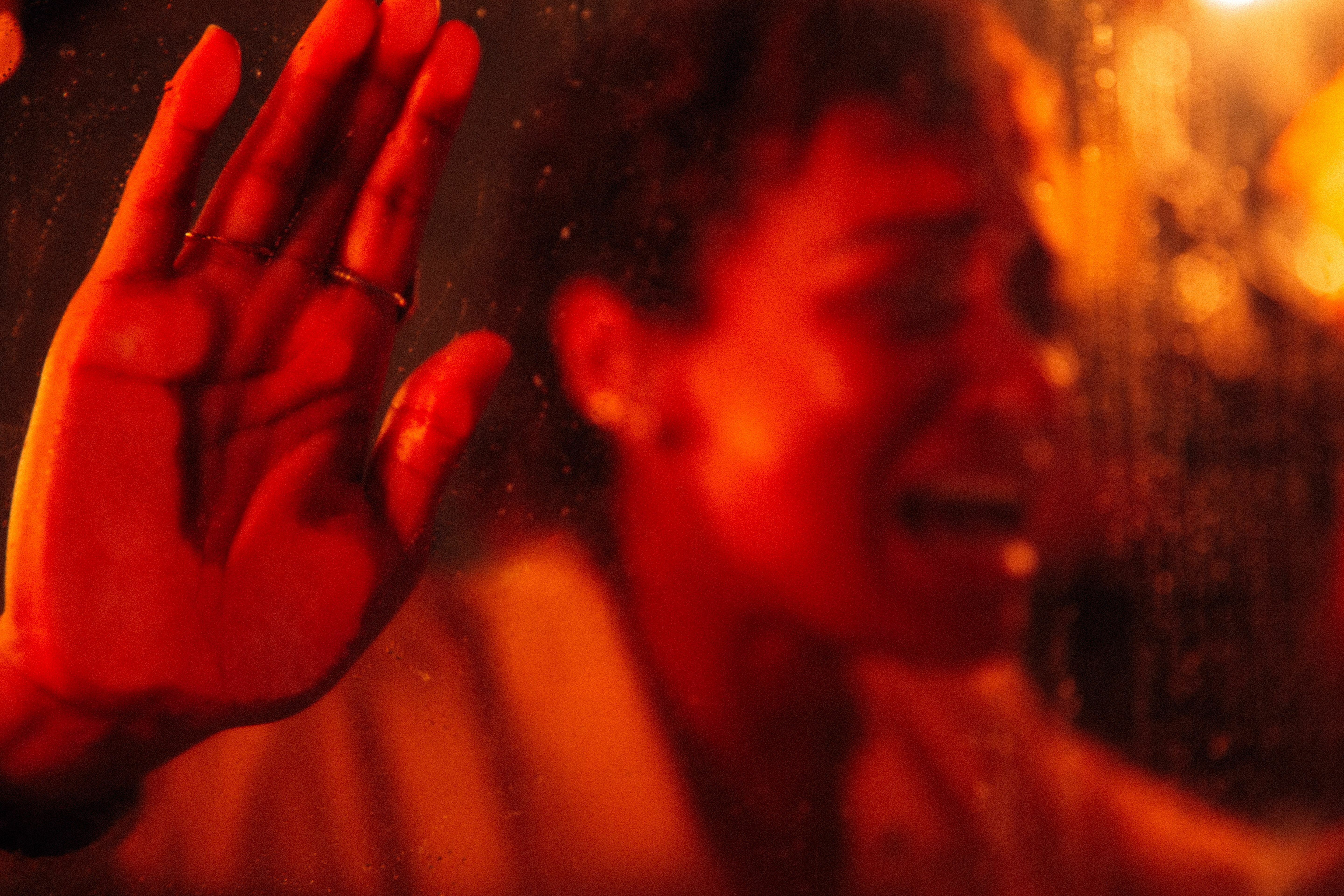A woman presses her hand and face against a window and screams, bathed in red lighting.