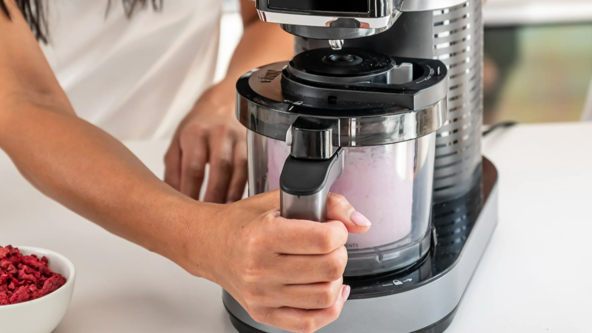 Hand grabbing ice cream maker handle with pink ice cream inside the jar