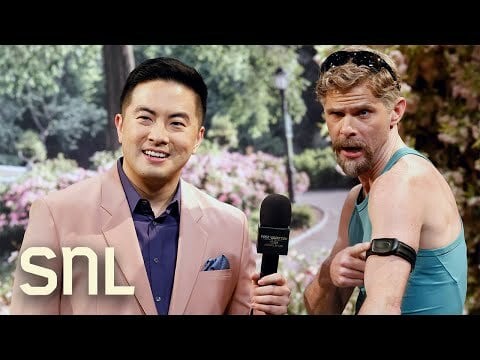 Bowen Yang in a salmon suit interviewing Mikey Day who's wearing tight spandex and a heart monitor on his left arm.