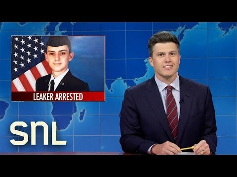 Weekend Update host Colin Jost next to a chyron of Airman Jake Teixeira