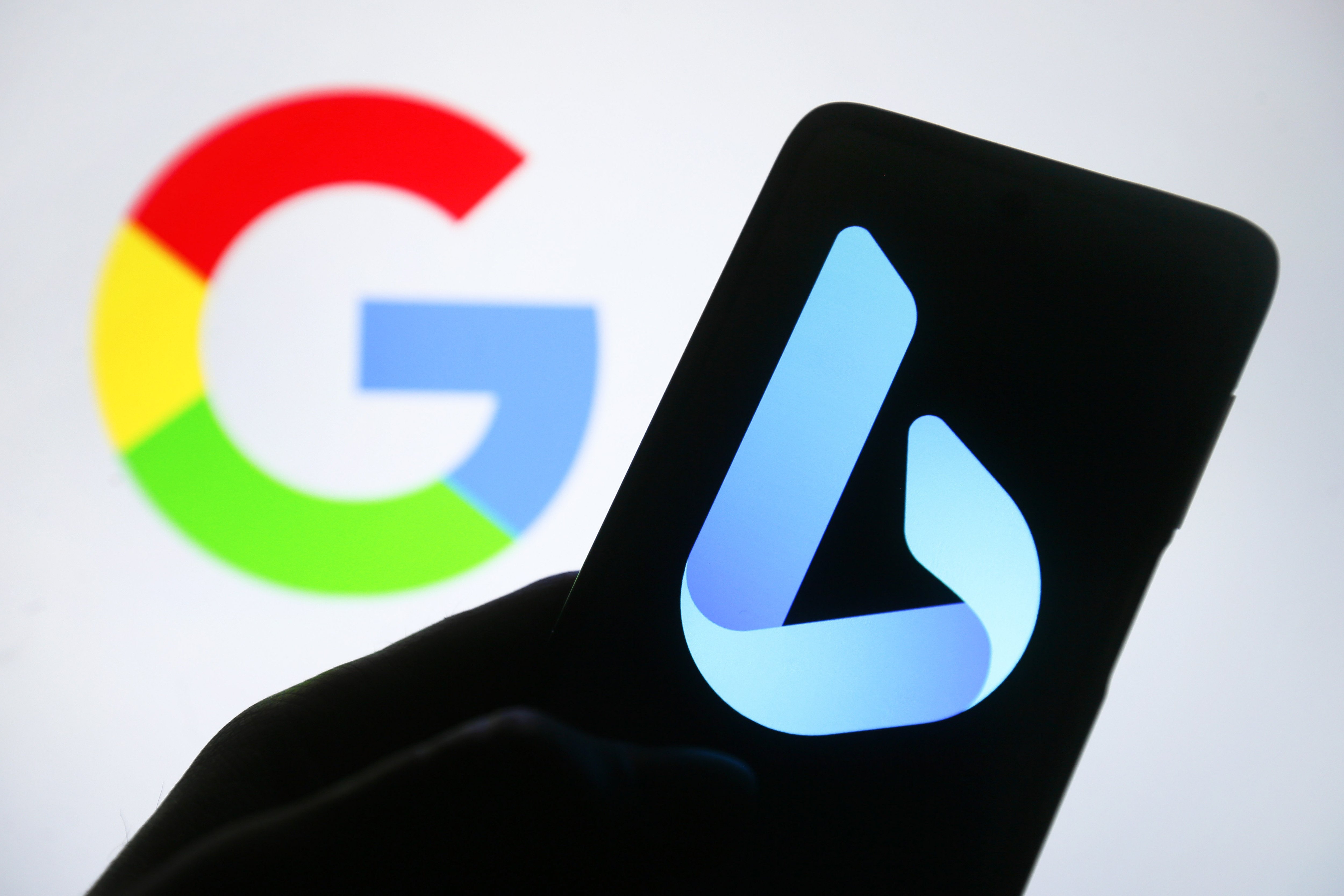 A silhouetted hand holds a phone with the blue Bing logo on the screen. Behind the phone is a Google logo in the background.